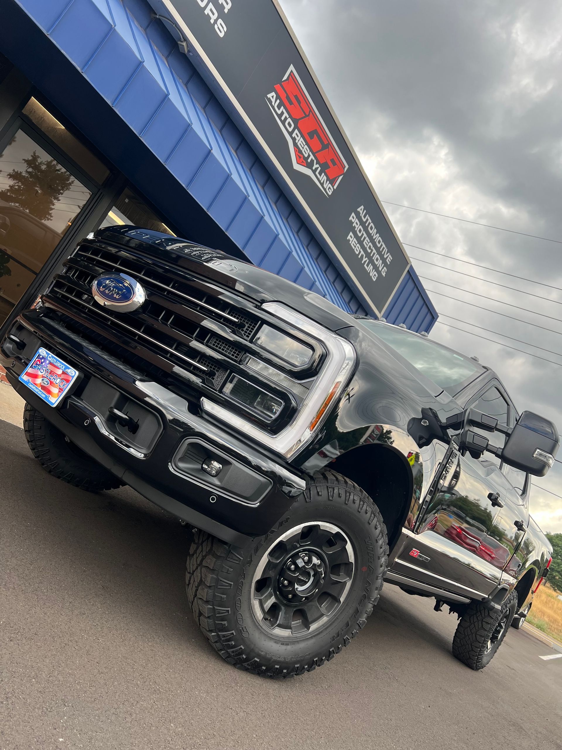 Black Ford truck parked in front of a building with red and white signage under a cloudy sky.