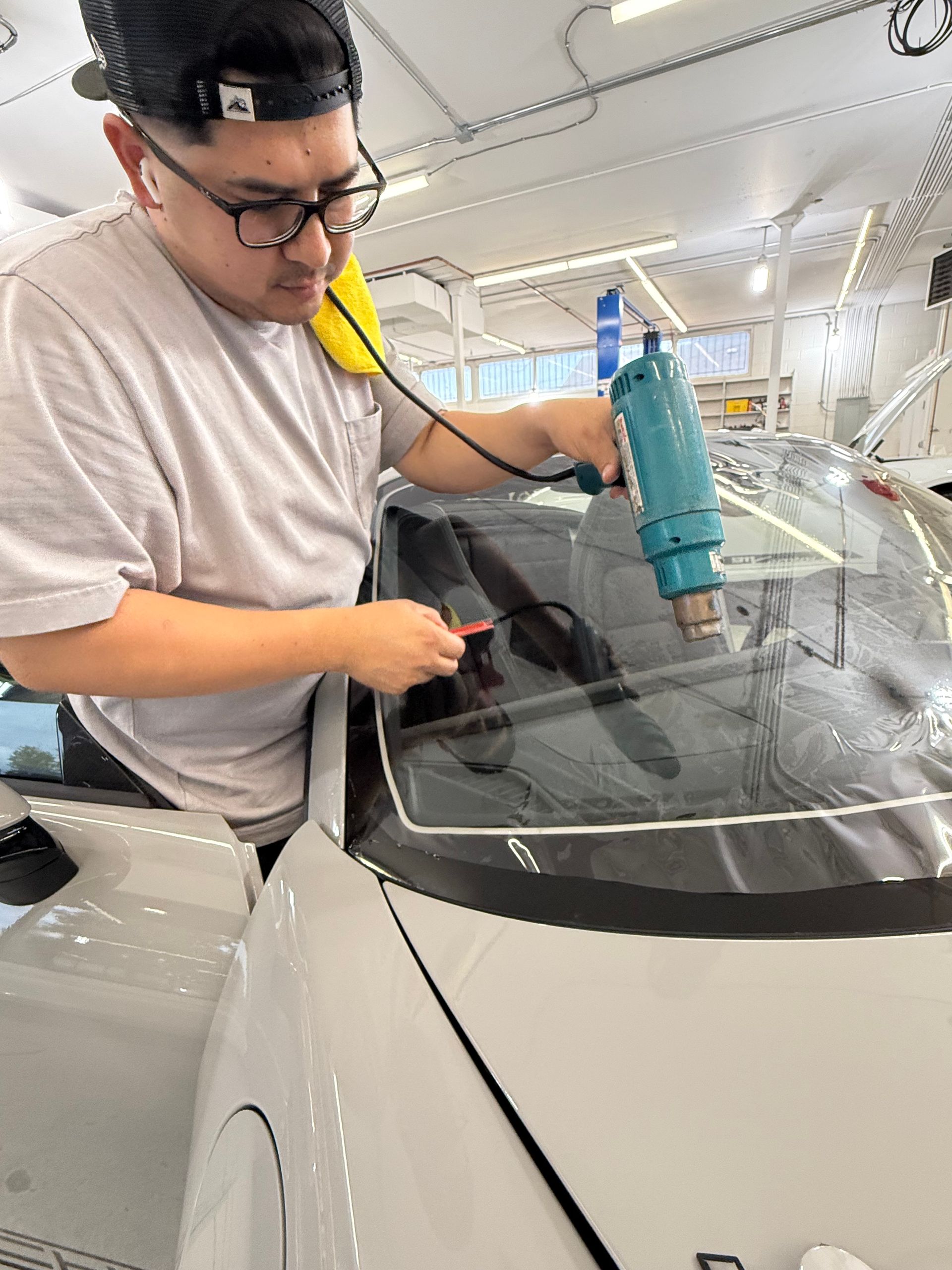 A person applying tint to a car window with a heat gun in a shop.