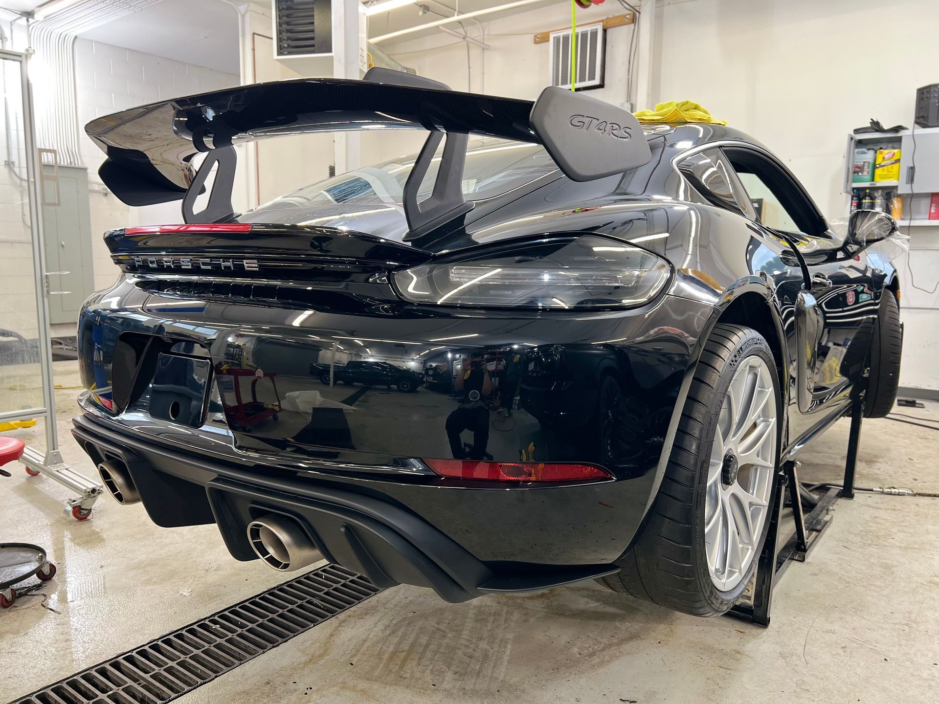 Black Porsche sports car with large rear wing, indoors, raised on a lift.