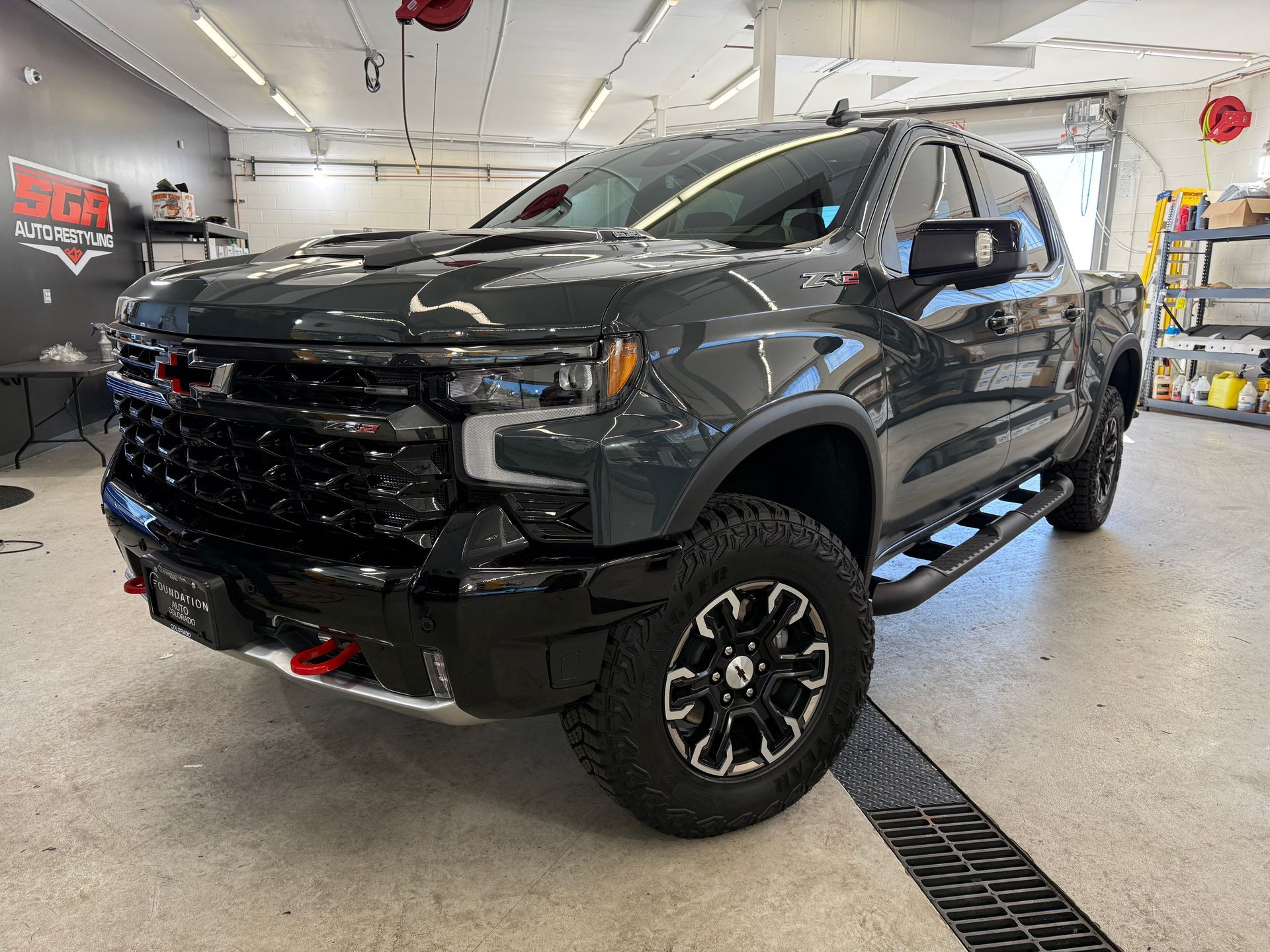 Dark gray Chevrolet truck with black grill and off-road tires, parked inside a garage.