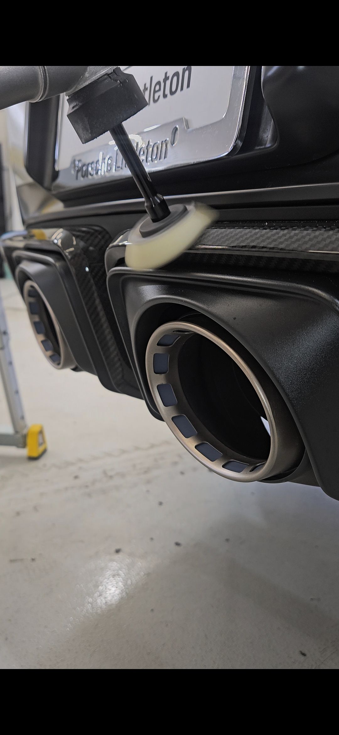 A person cleaning the exhaust pipe of a black car with a brush.