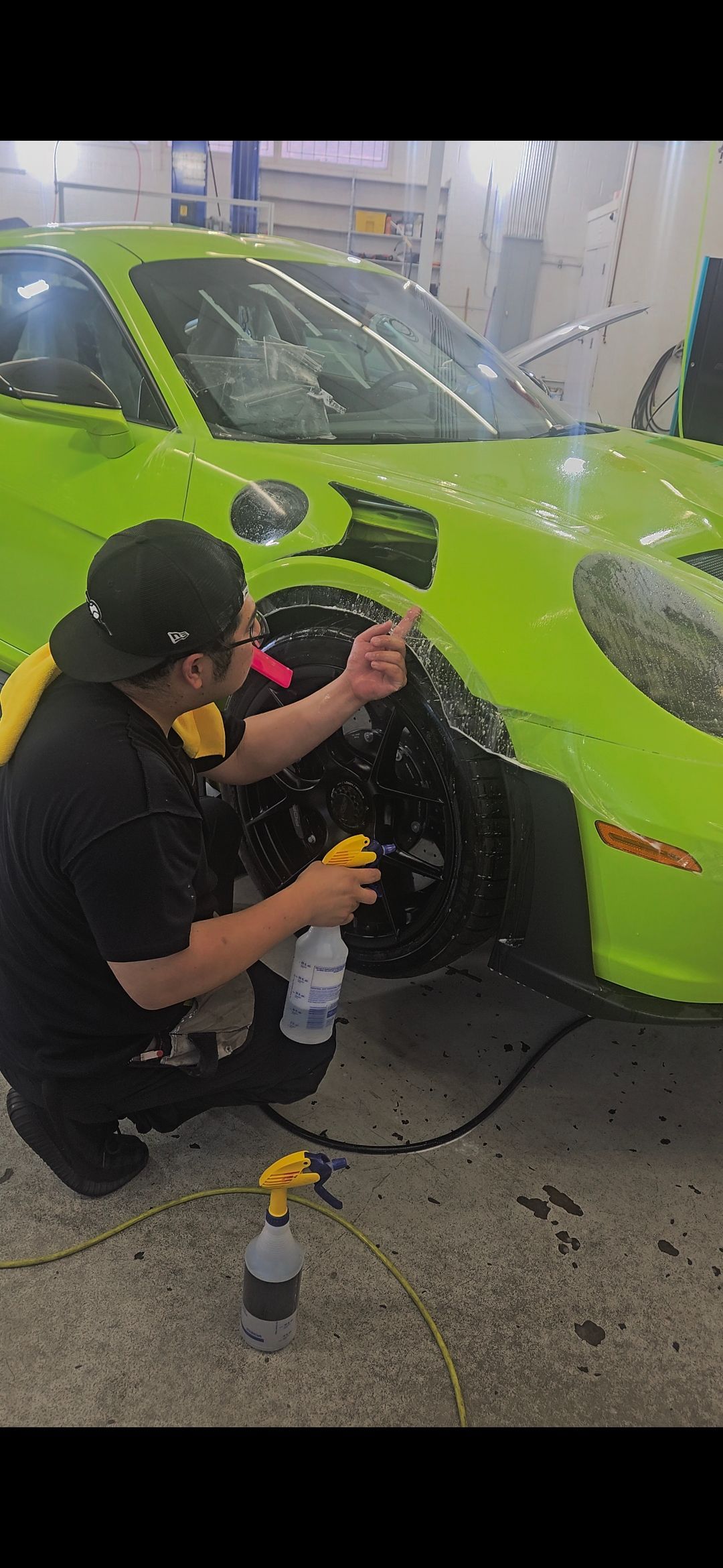 Person sprays a green sports car. They are kneeling in front of the tire applying a protective coating.