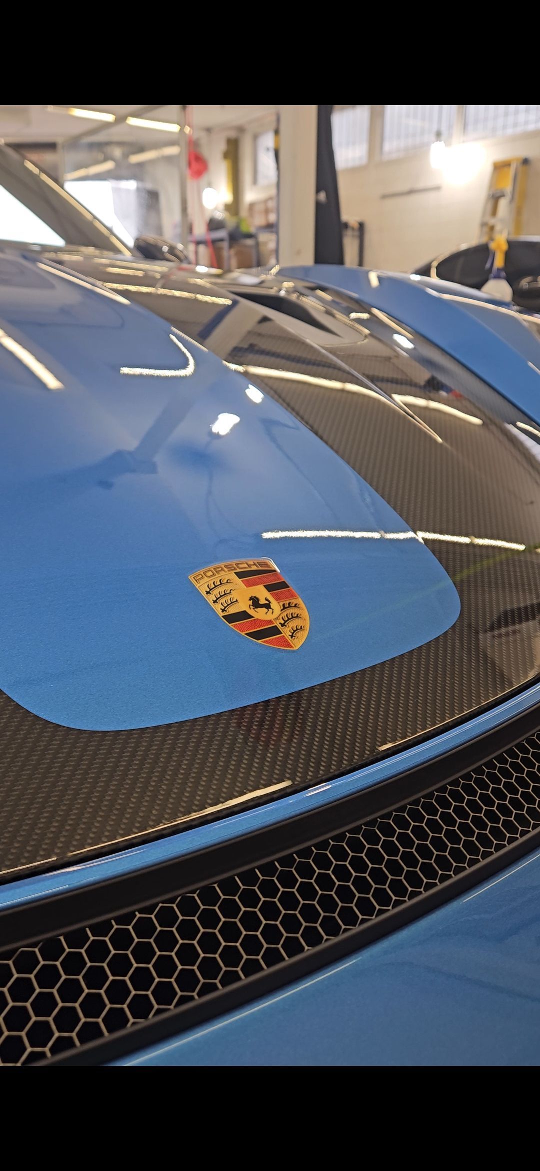 Blue Porsche car hood with emblem, carbon fiber elements, and honeycomb grille.