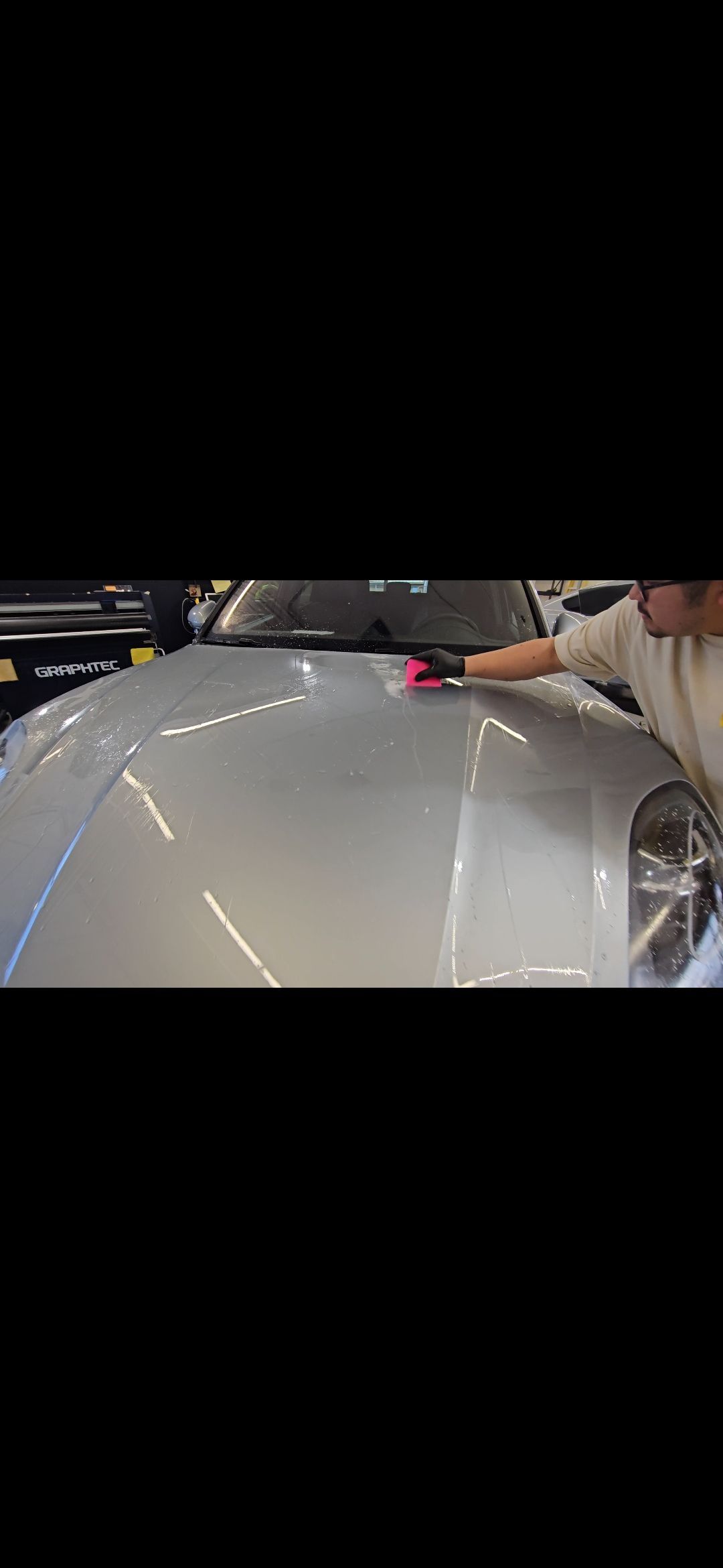 Person applying product to a silver car hood with a pink applicator, indoors.