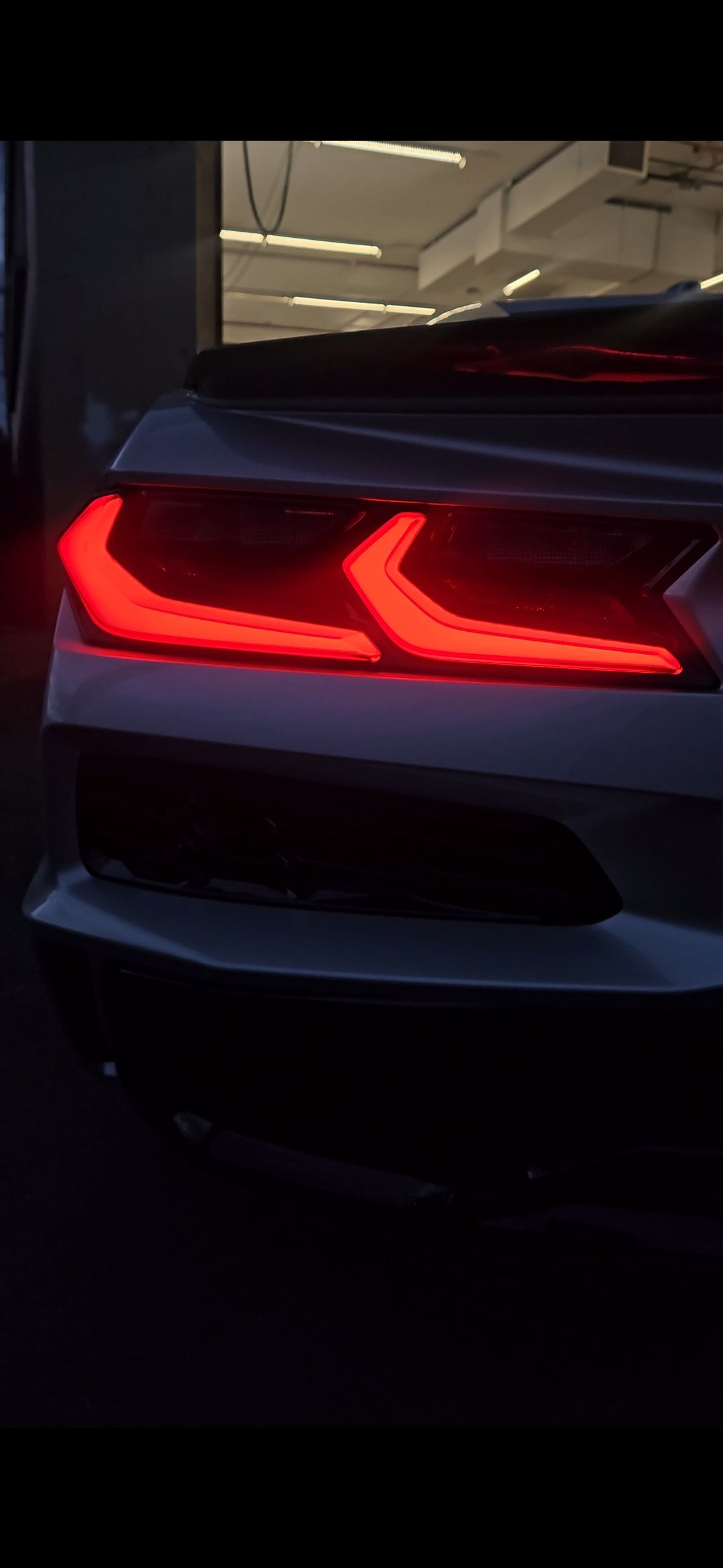 Rear of a white car with bright red taillights illuminated in a dark setting.