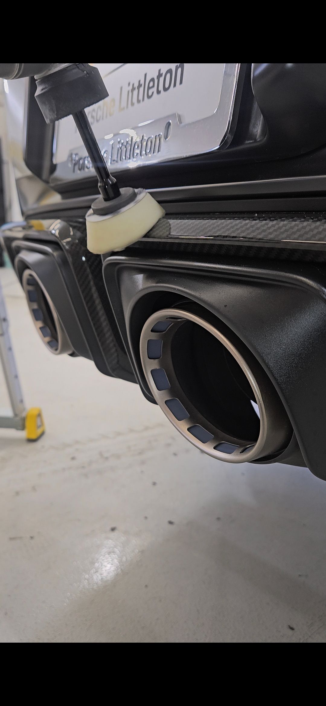 Close-up of a car's exhaust pipes being polished with a buffing tool.