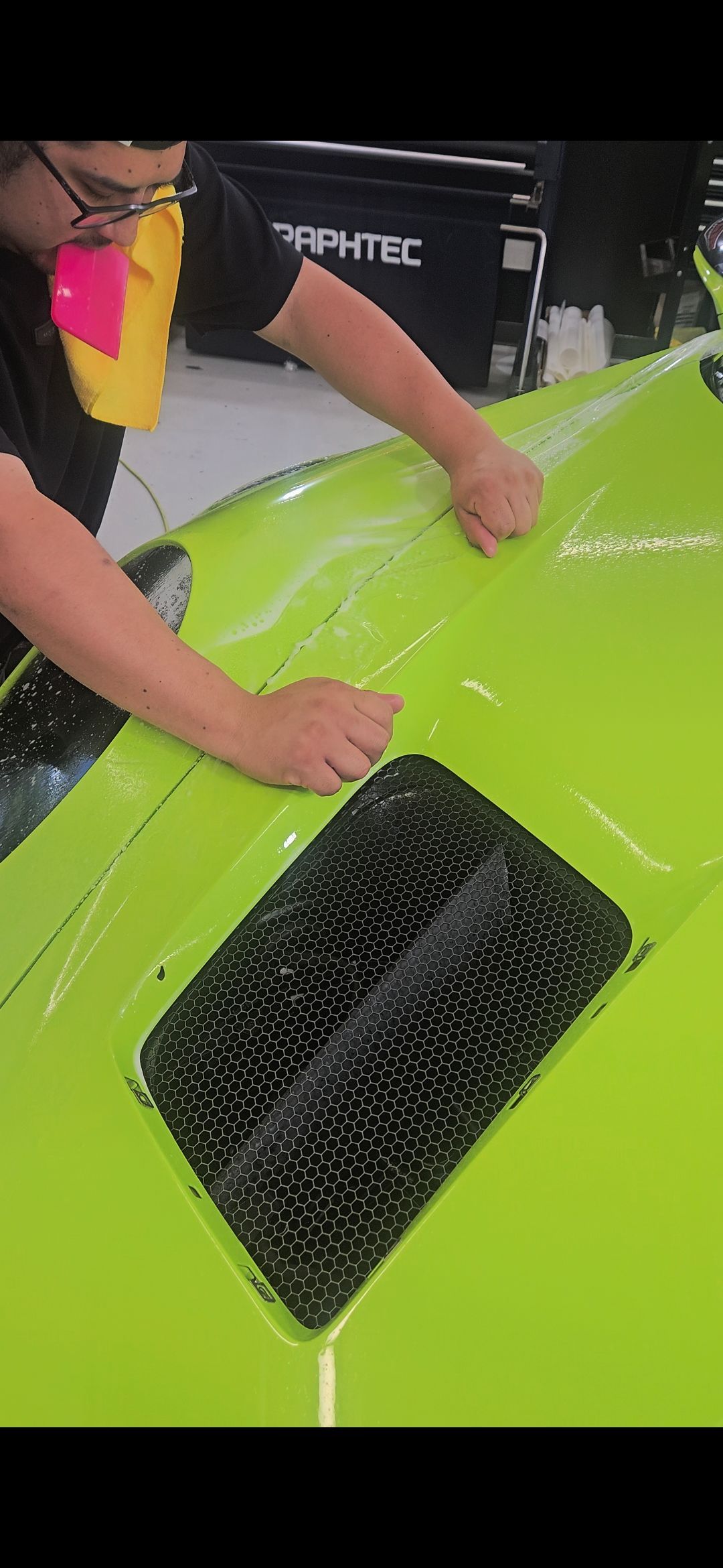 A person applies film to a neon green car hood with a black vent.