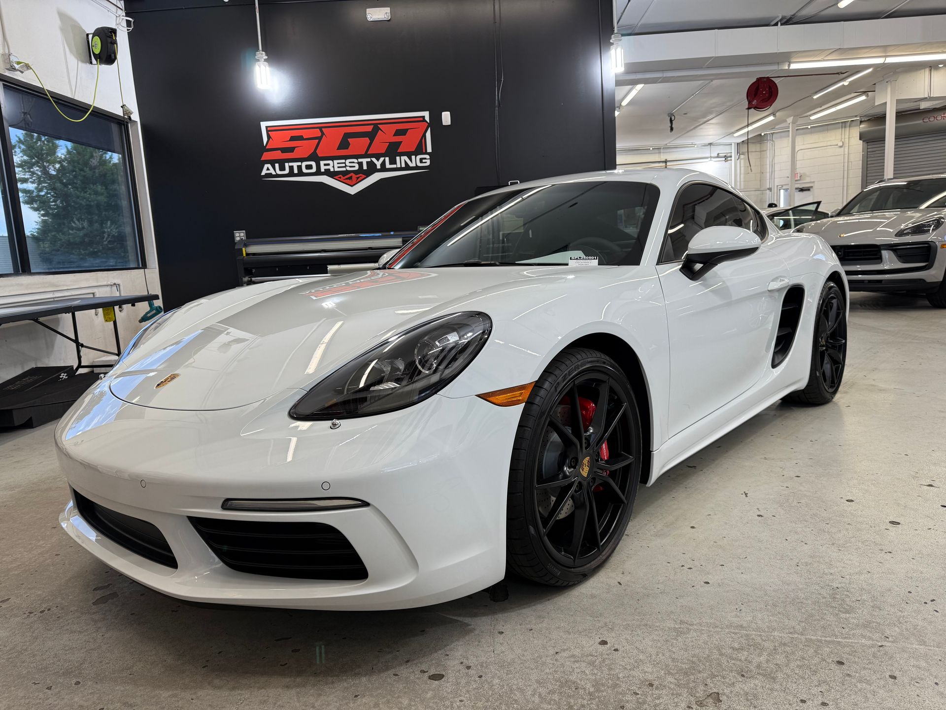 White Porsche sports car in a shop. Black rims and red brake calipers are visible. 