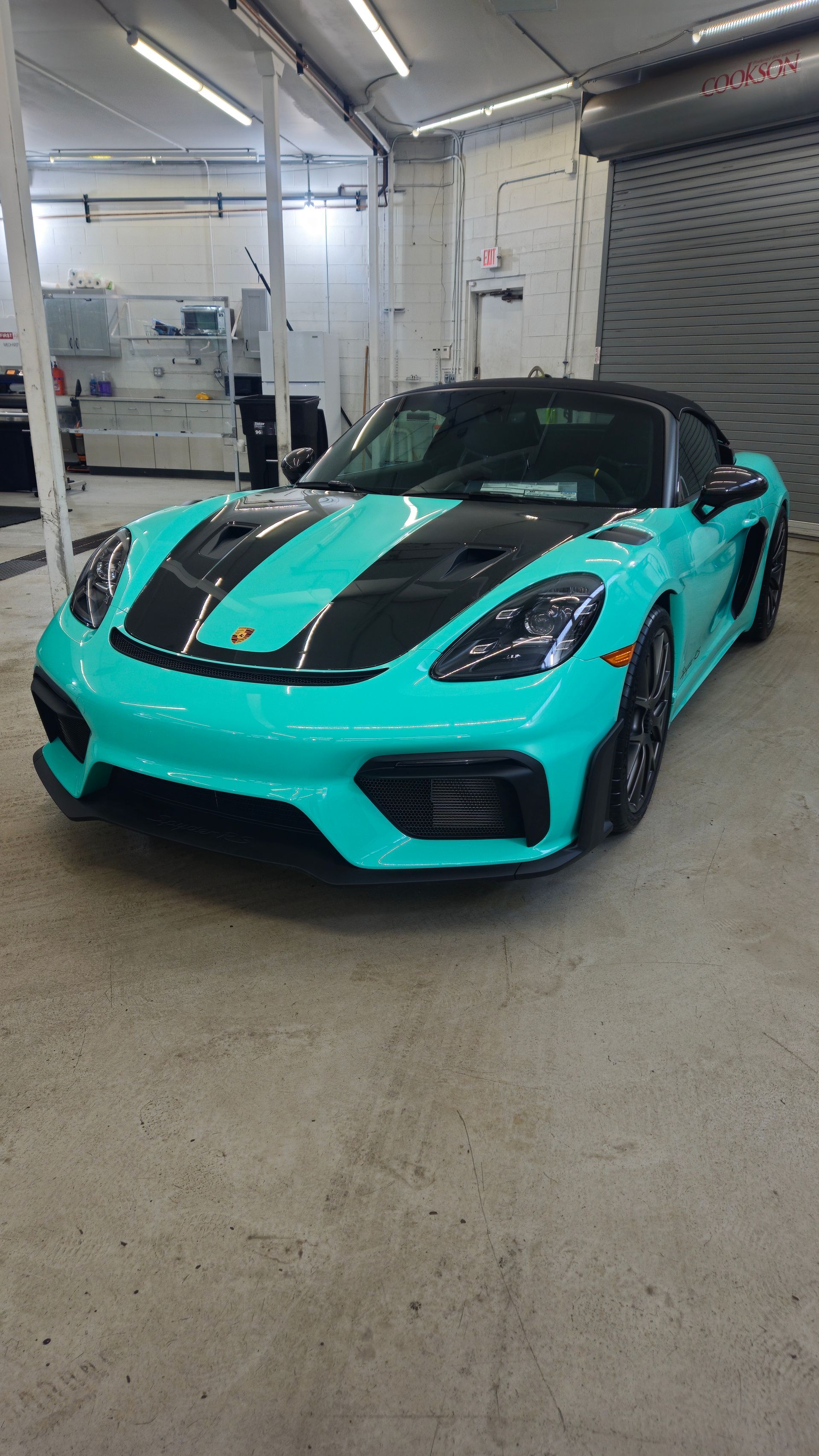 Teal Porsche sports car with black racing stripes in a garage.