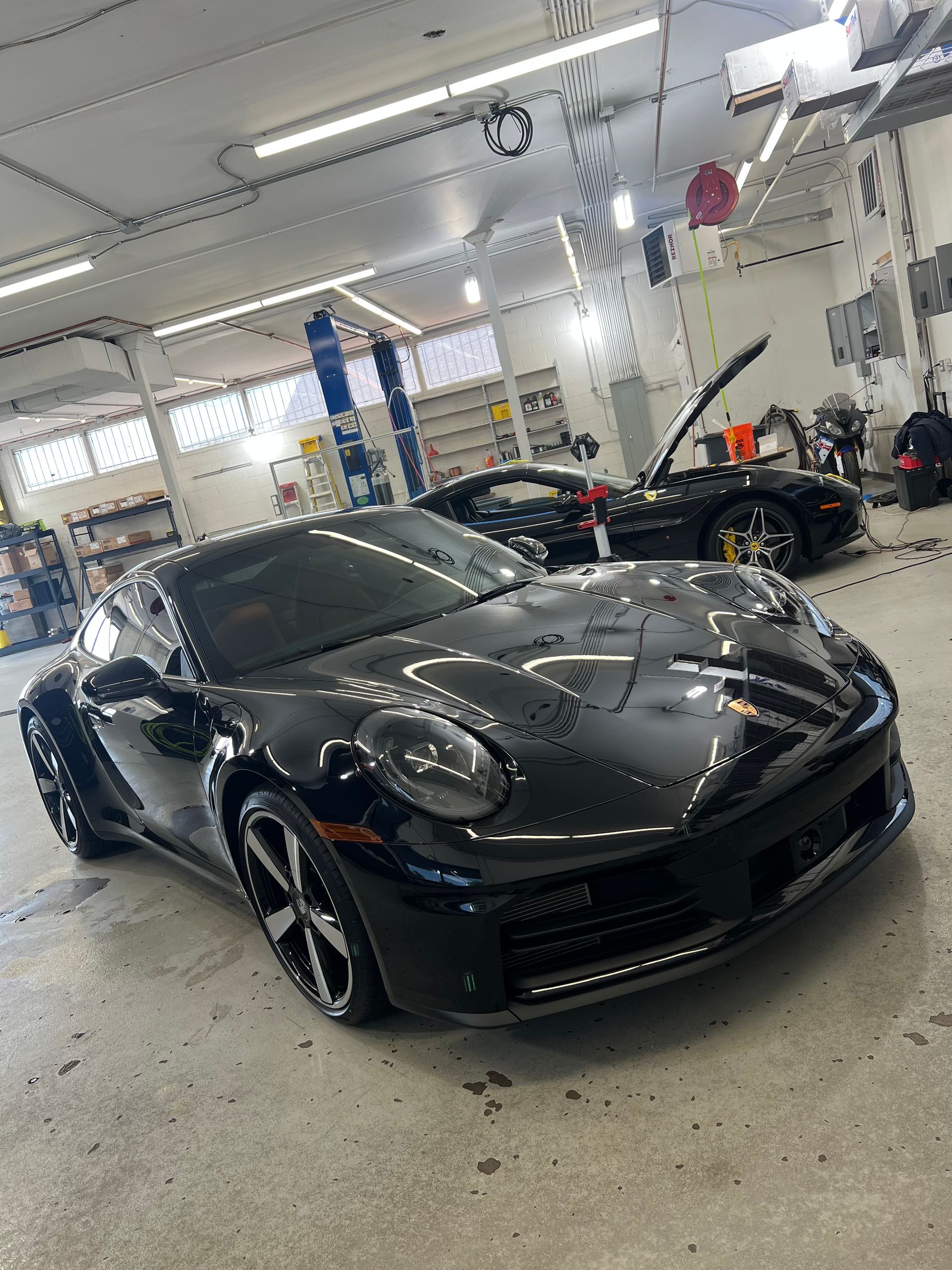 Black Porsche sports car in a garage with another black car in the background. Garage interior, bright lights.