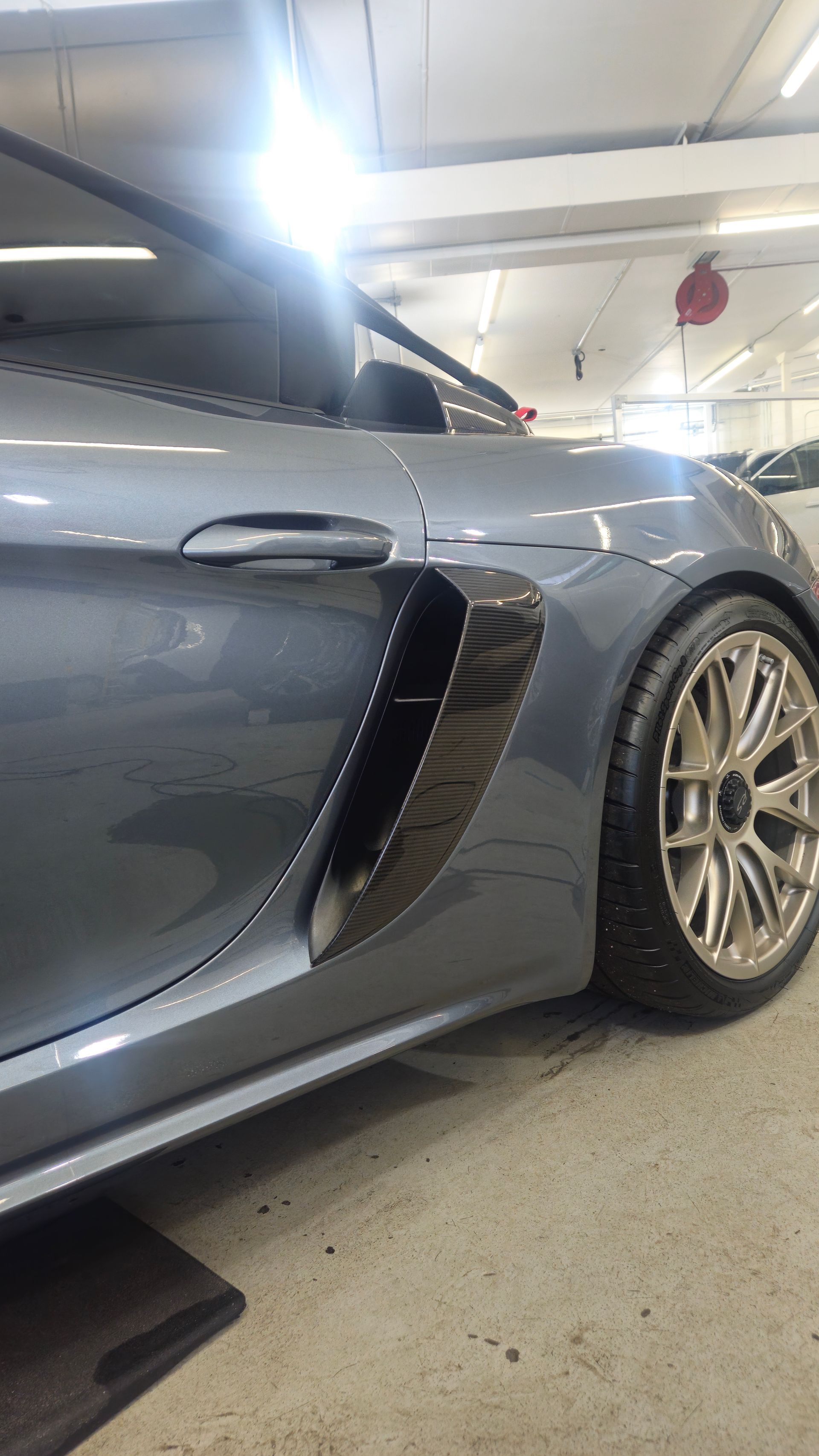Gray Porsche sports car with carbon fiber side vent, parked indoors.
