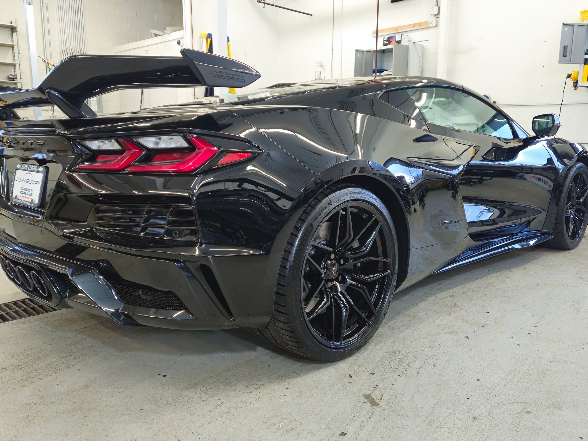 Black Chevrolet Corvette sports car with a large rear wing, parked indoors.