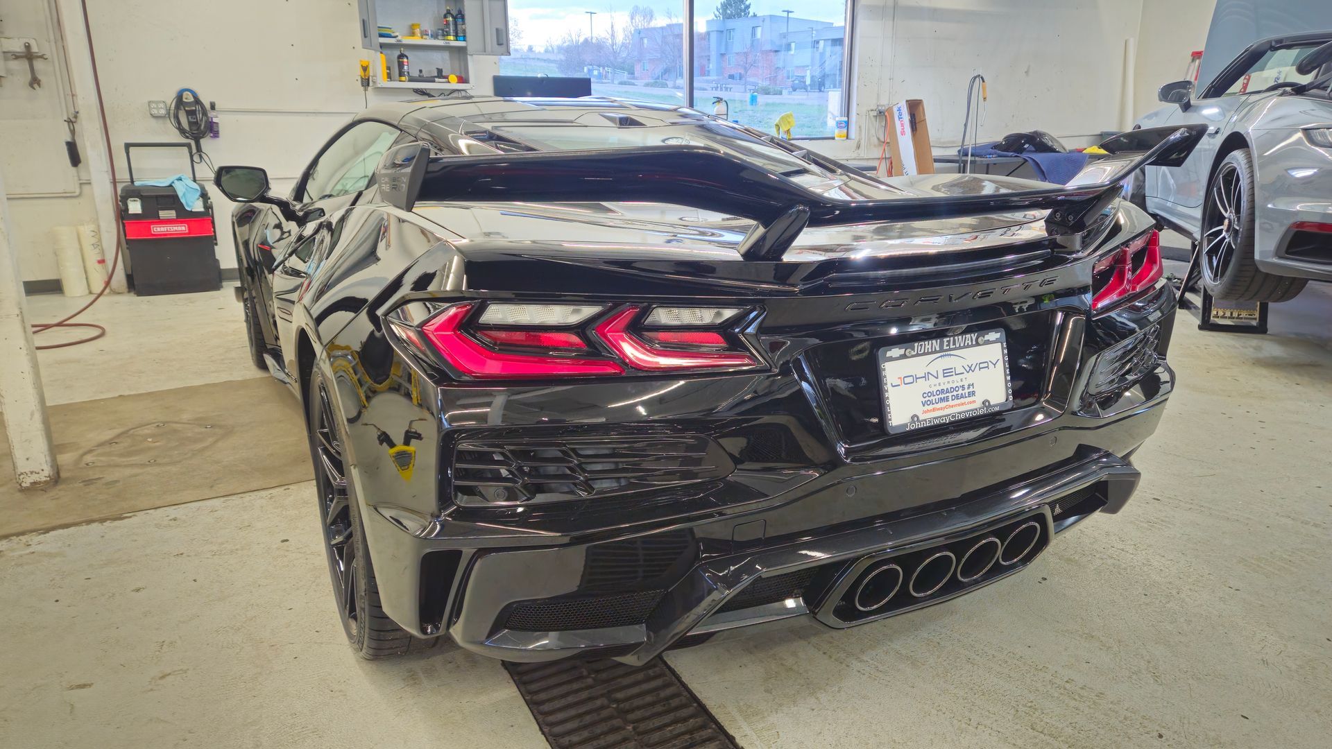 Black Chevrolet Corvette in a garage, showcasing its rear design with taillights and exhaust.