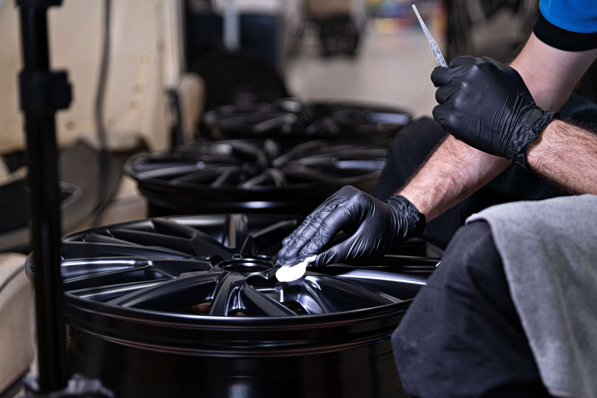 Hands in black gloves applying a blue sponge to a black car door with a spray bottle.