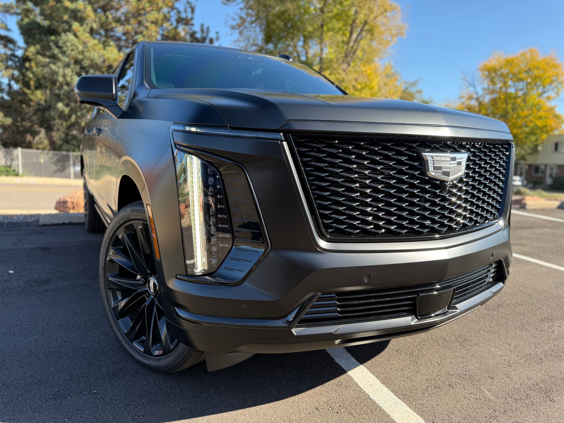Black Cadillac SUV with black grill and wheels, parked outdoors on a sunny day.