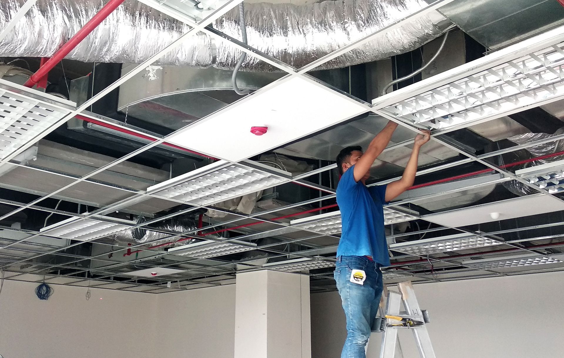 A man is standing on a ladder working on a ceiling.
