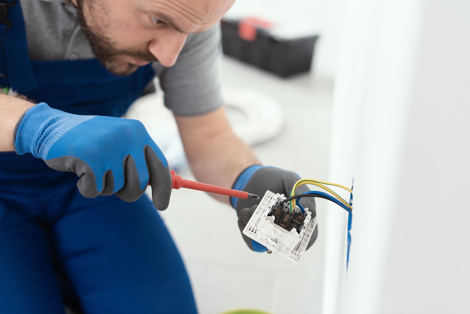 A man is fixing an electrical outlet on a wall with a screwdriver.