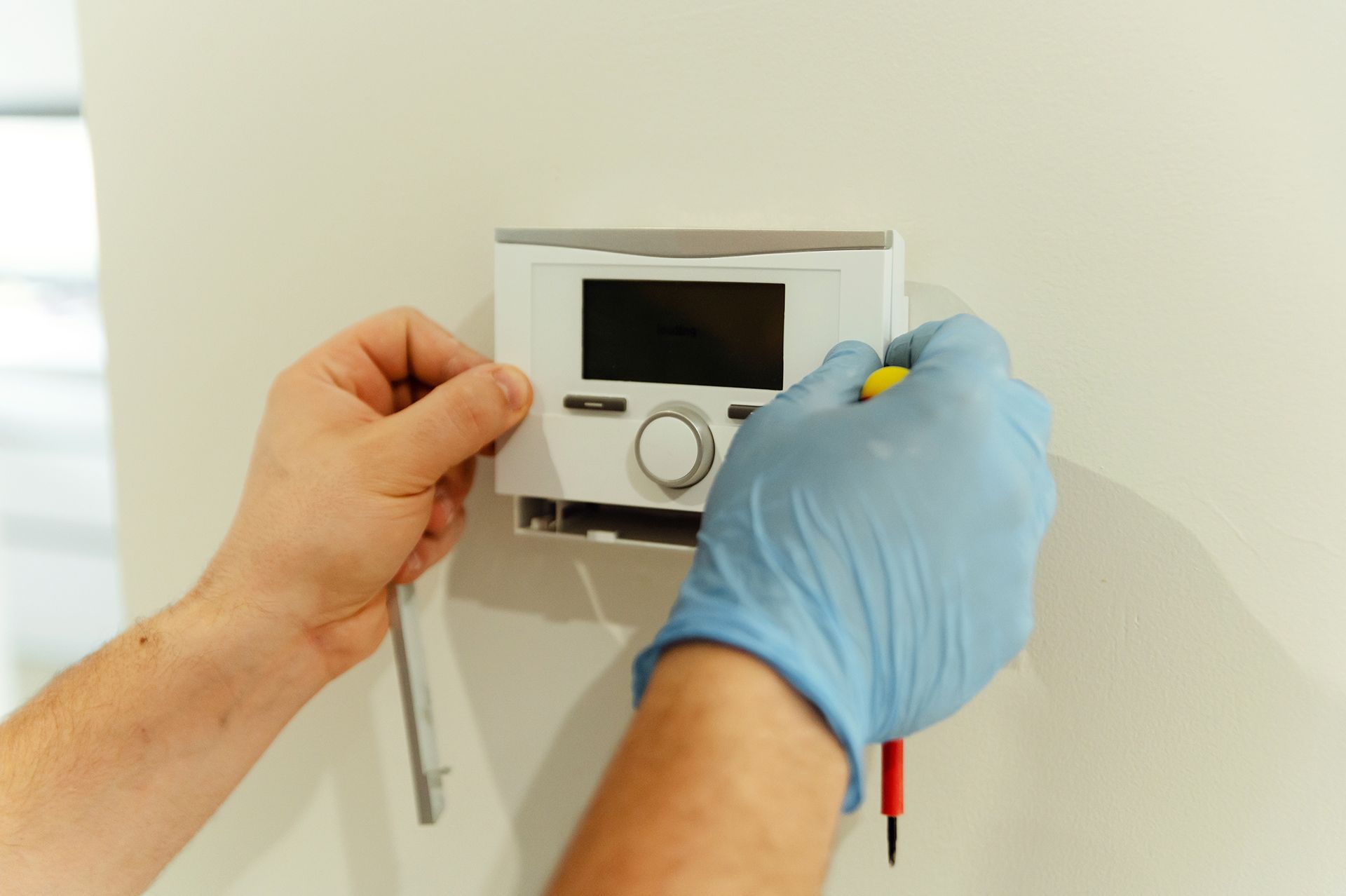 A person wearing blue gloves is installing a thermostat on a wall