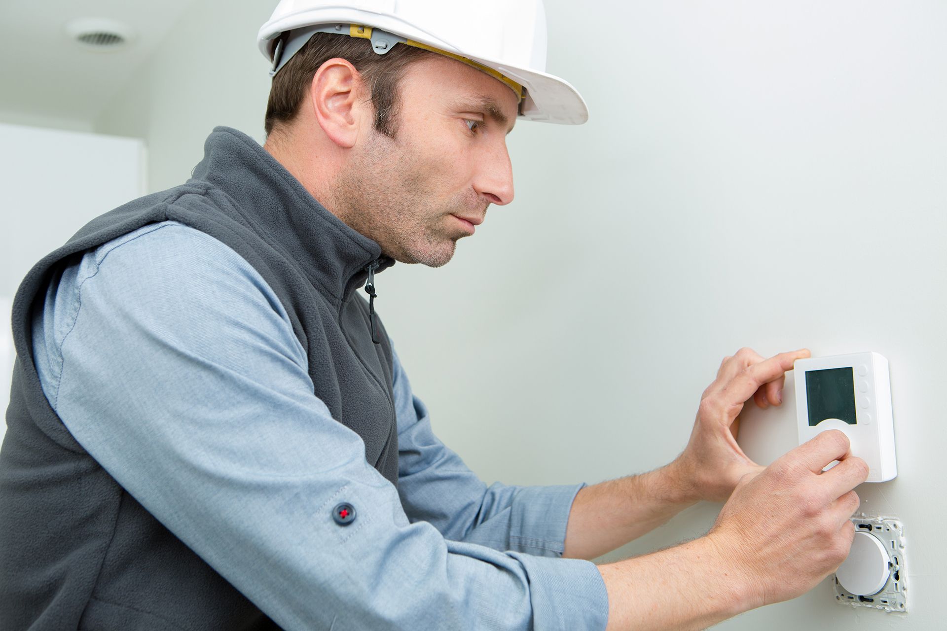 A man in a hard hat is adjusting a thermostat on a wall