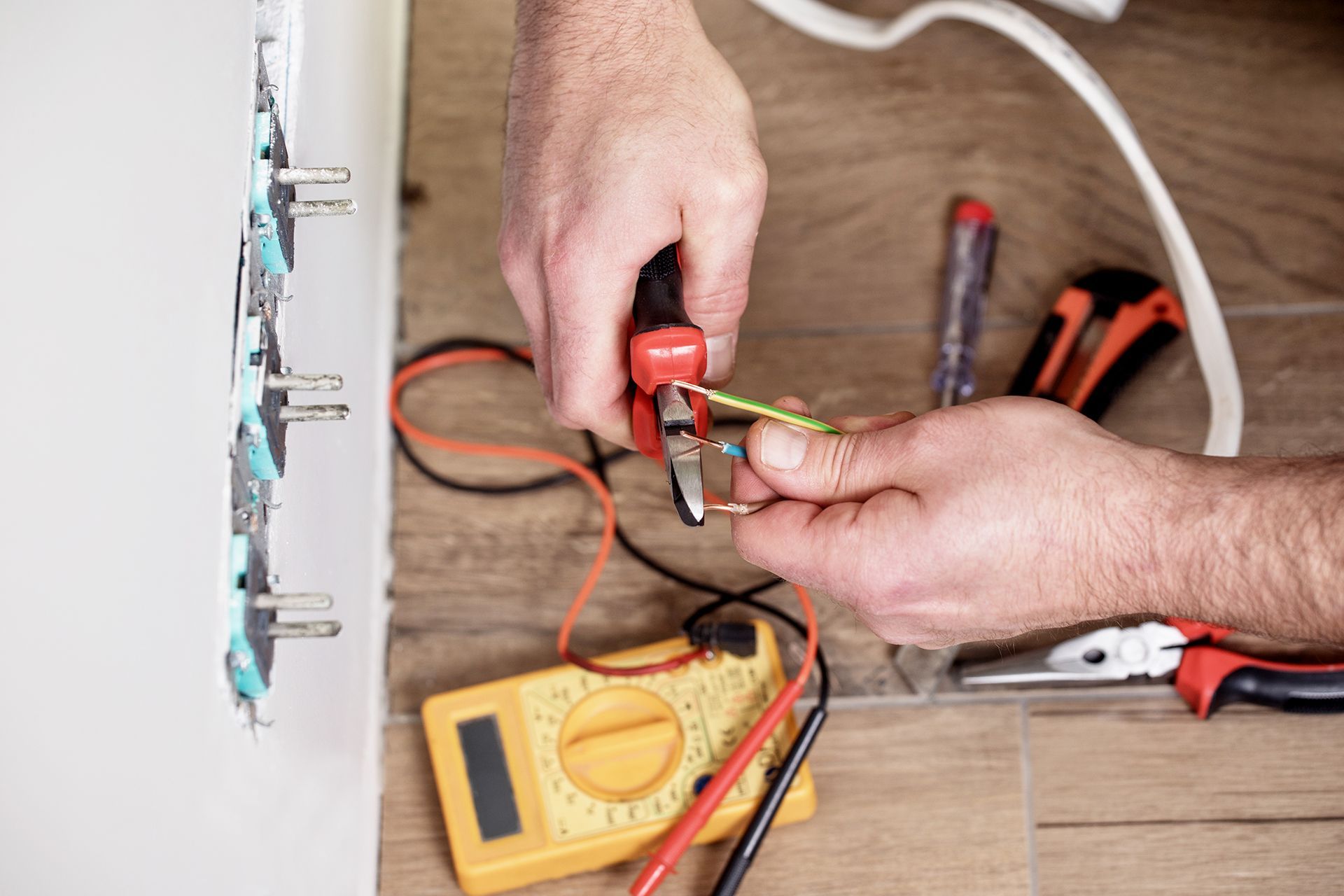 A man is working on an electric outlet with a pair of pliers