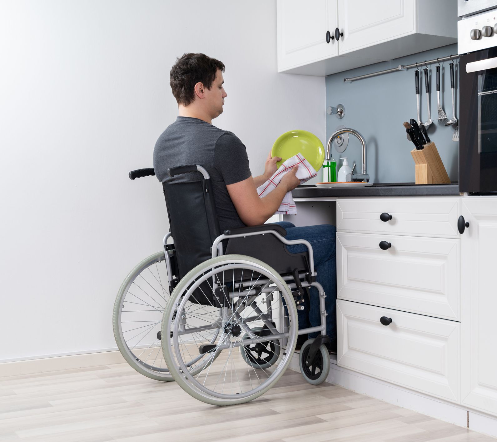 Man in wheelchair washing dishes at a modified kitchen sink.