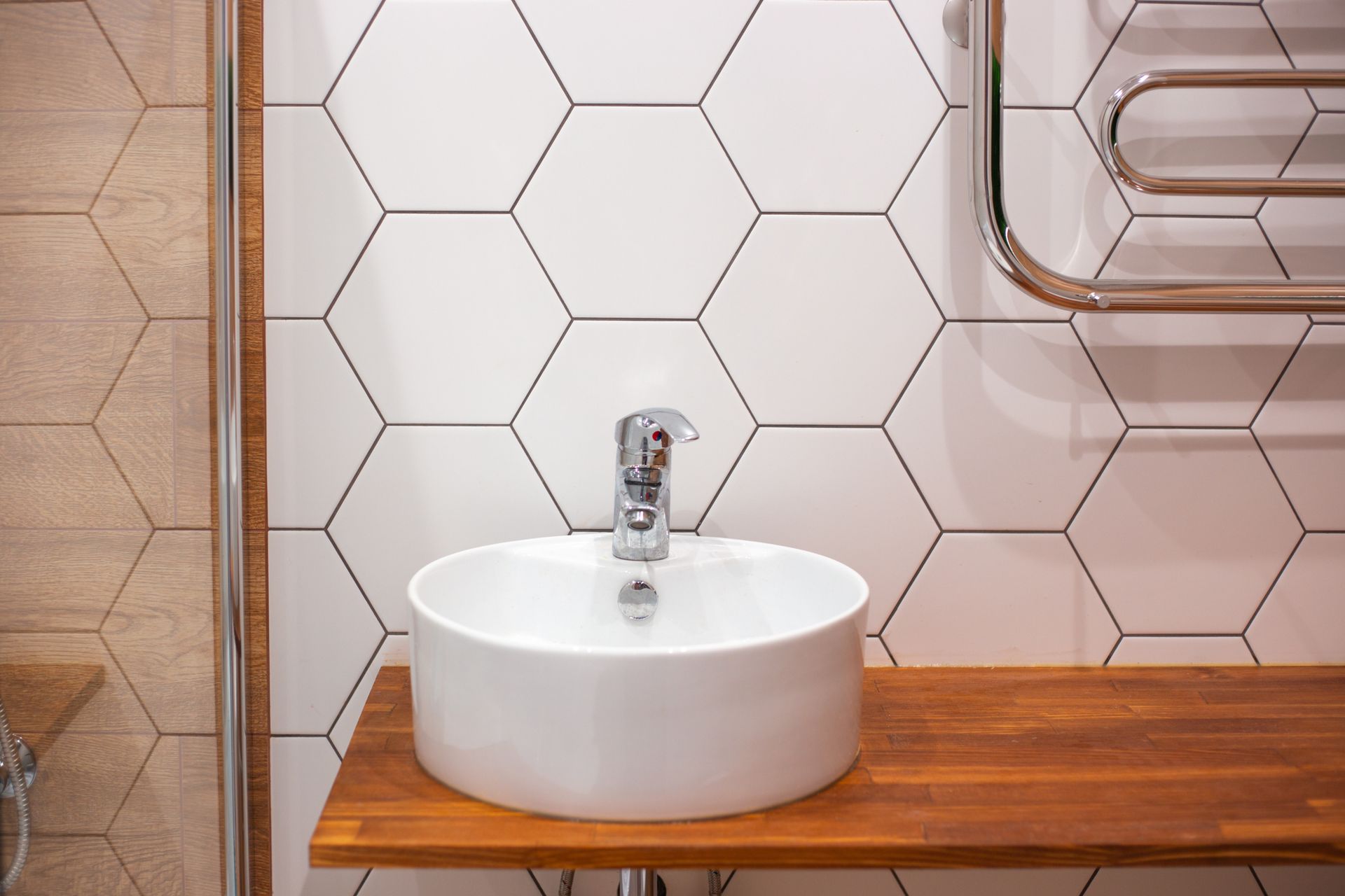 White round sink on wooden shelf, surrounded by white hexagon tiles; towel rack above.