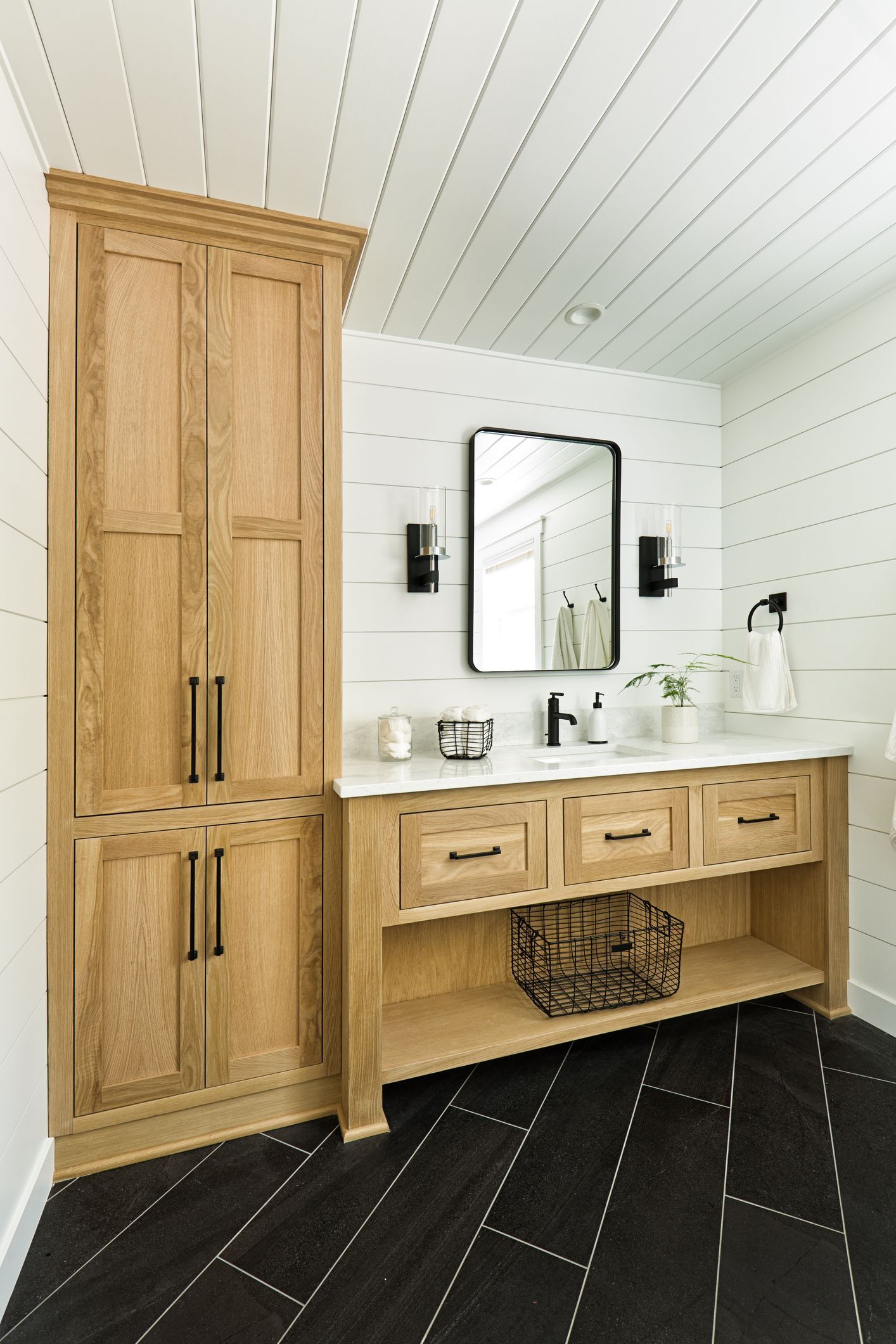 Bathroom with wood vanity, black and white tile, and a tall storage cabinet.