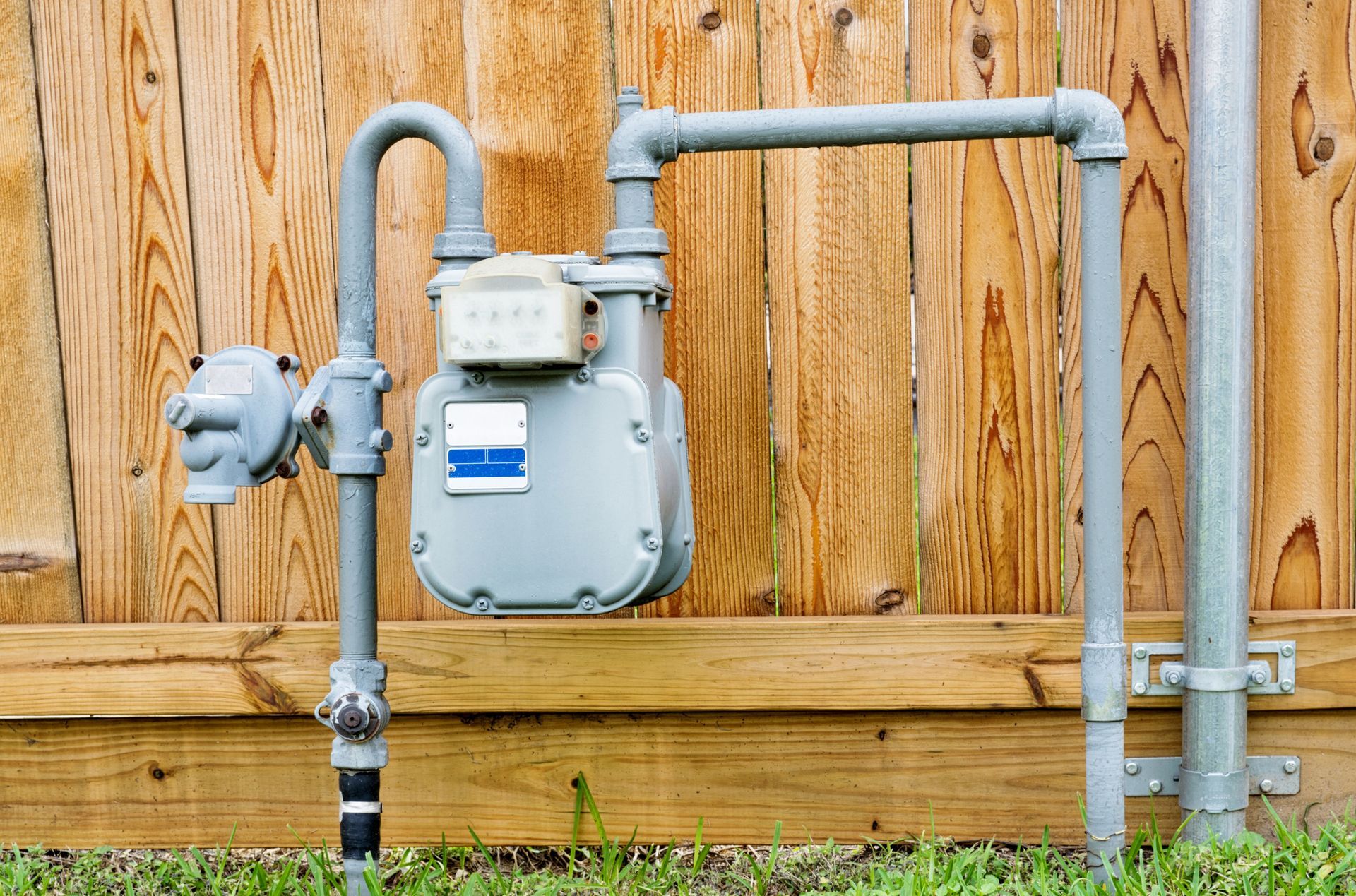 Gas meter on wooden fence, with grey pipes and regulator.
