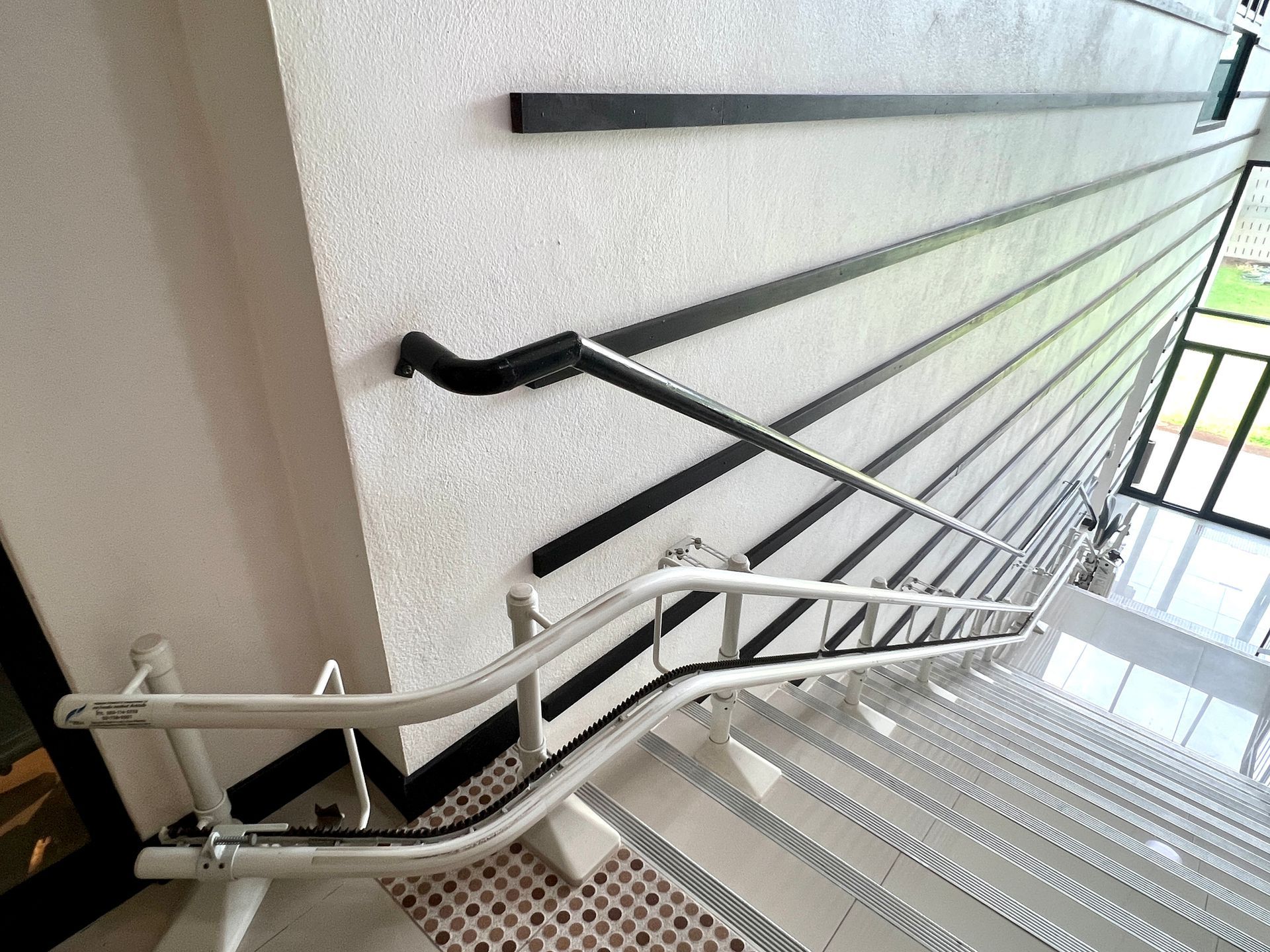 Handrails on staircase with black lines on the wall and a window in the background.