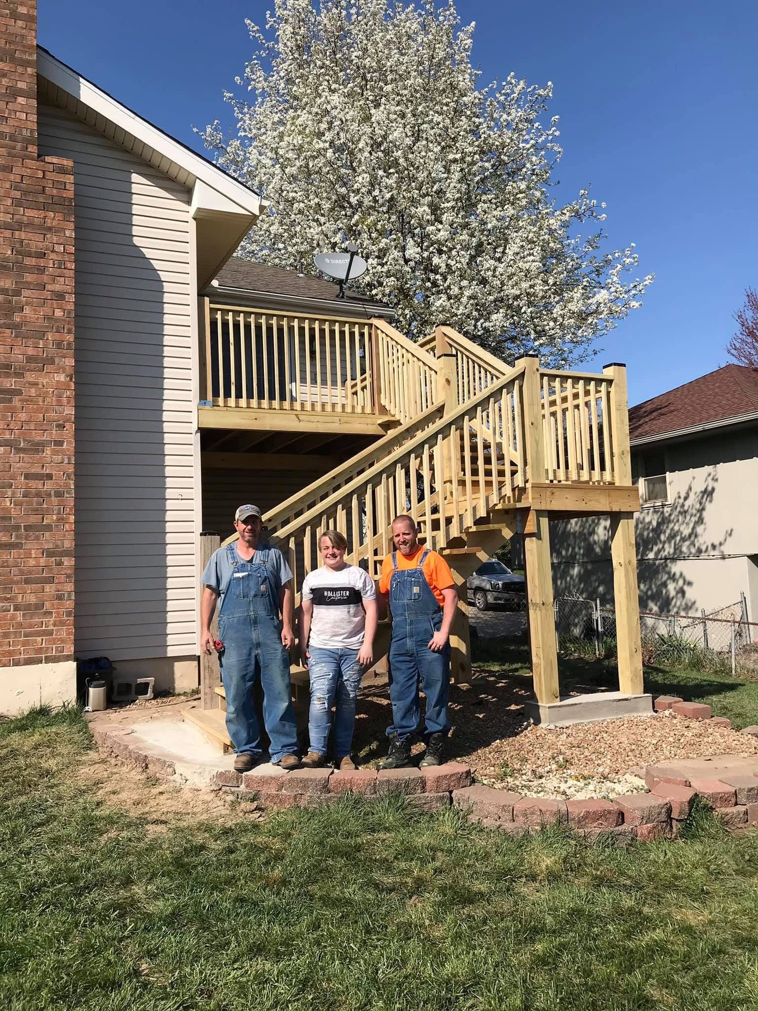 Man in overalls carrying pipe on shoulder in a yard, surrounded by more pipes.