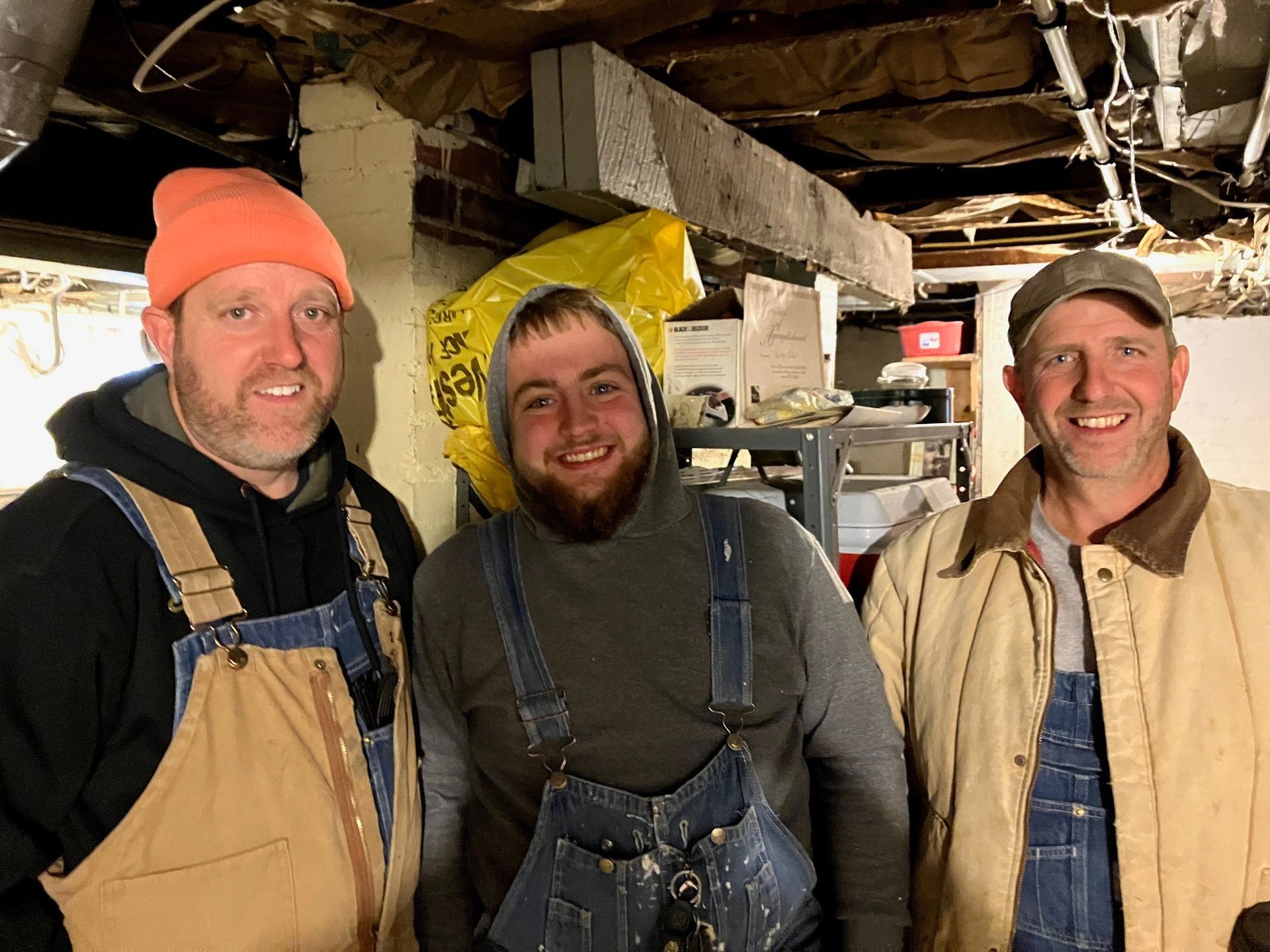 Black corrugated drain pipes lay on the ground beside a dug trench; AC unit and shovel near the building.