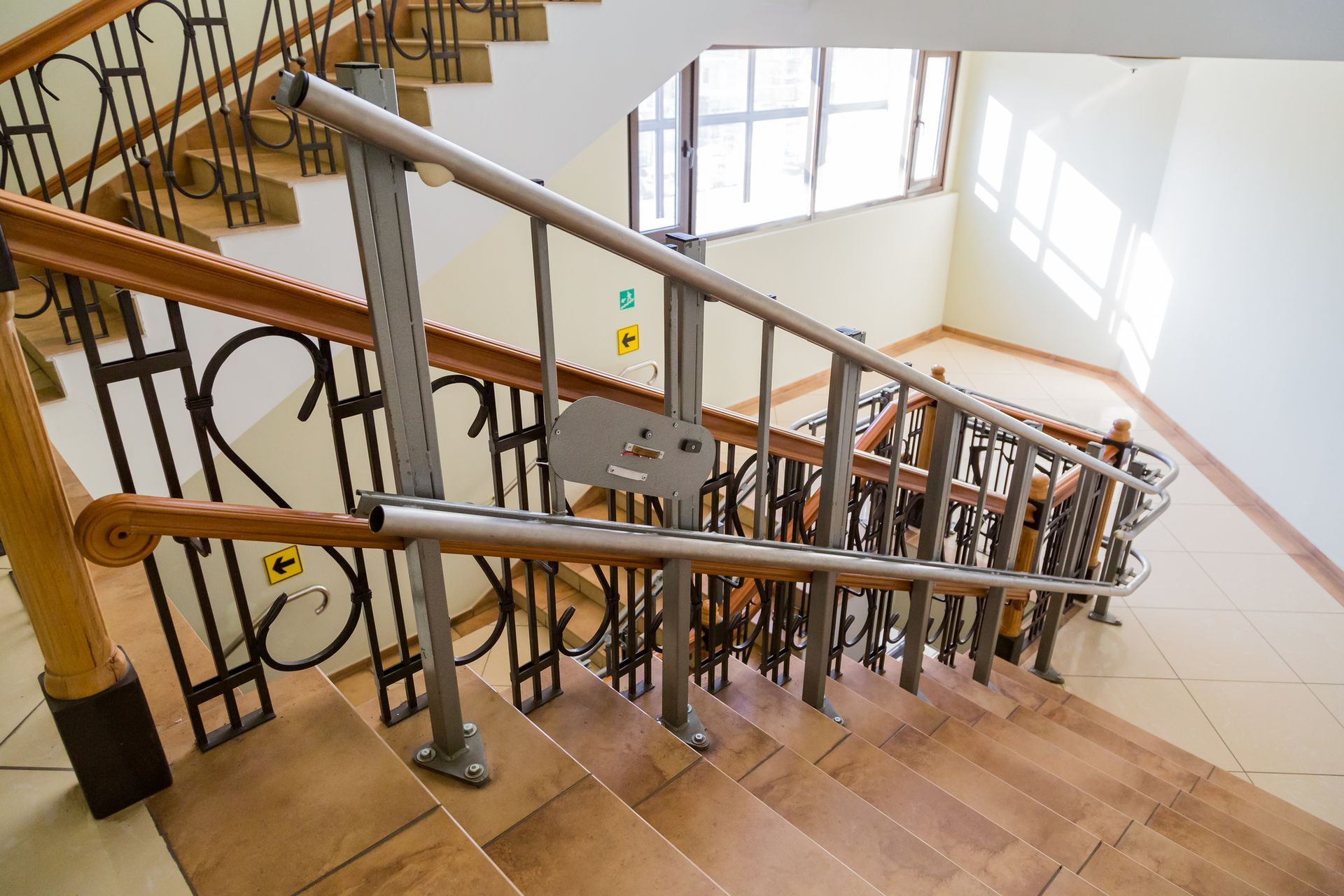 Staircase with a metal and wooden railing, and a stair lift. Windows in the background.