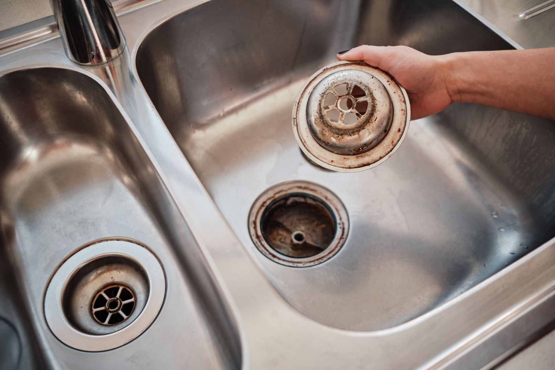 Hand removing sink strainer from stainless steel kitchen sink.
