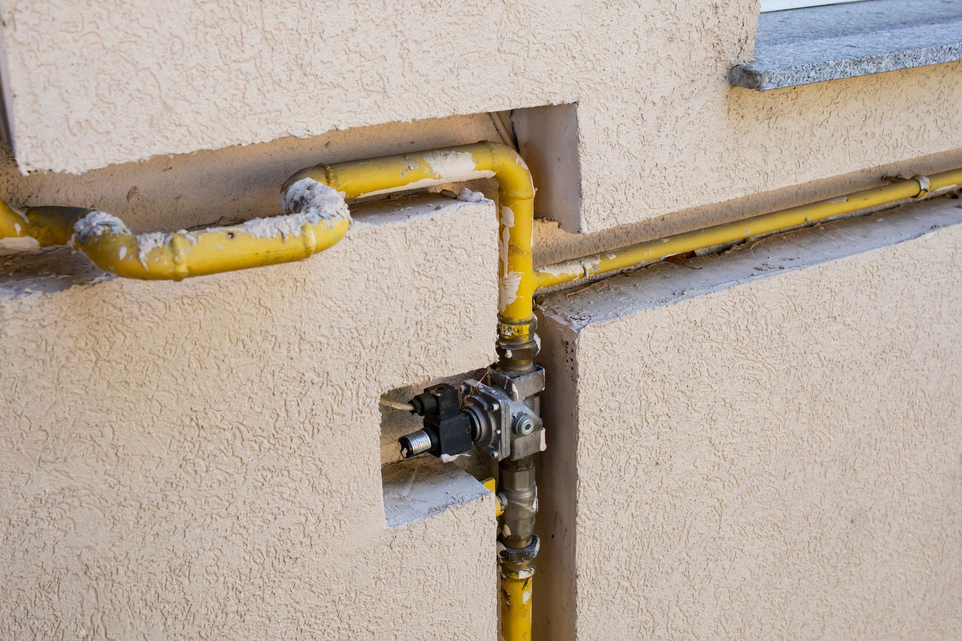 Yellow gas pipes on a beige stucco wall, with a regulator visible in a recessed area.