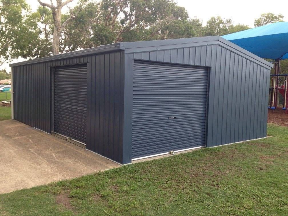 A Blue Garage With Roller Doors Is Sitting On Top Of A Lush Green Field — Just Sheds In Kunda Park, QLD