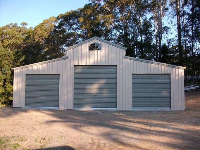 A Large Building With Three Garage Doors Is Surrounded By Trees — Just Sheds In Kunda Park, QLD
