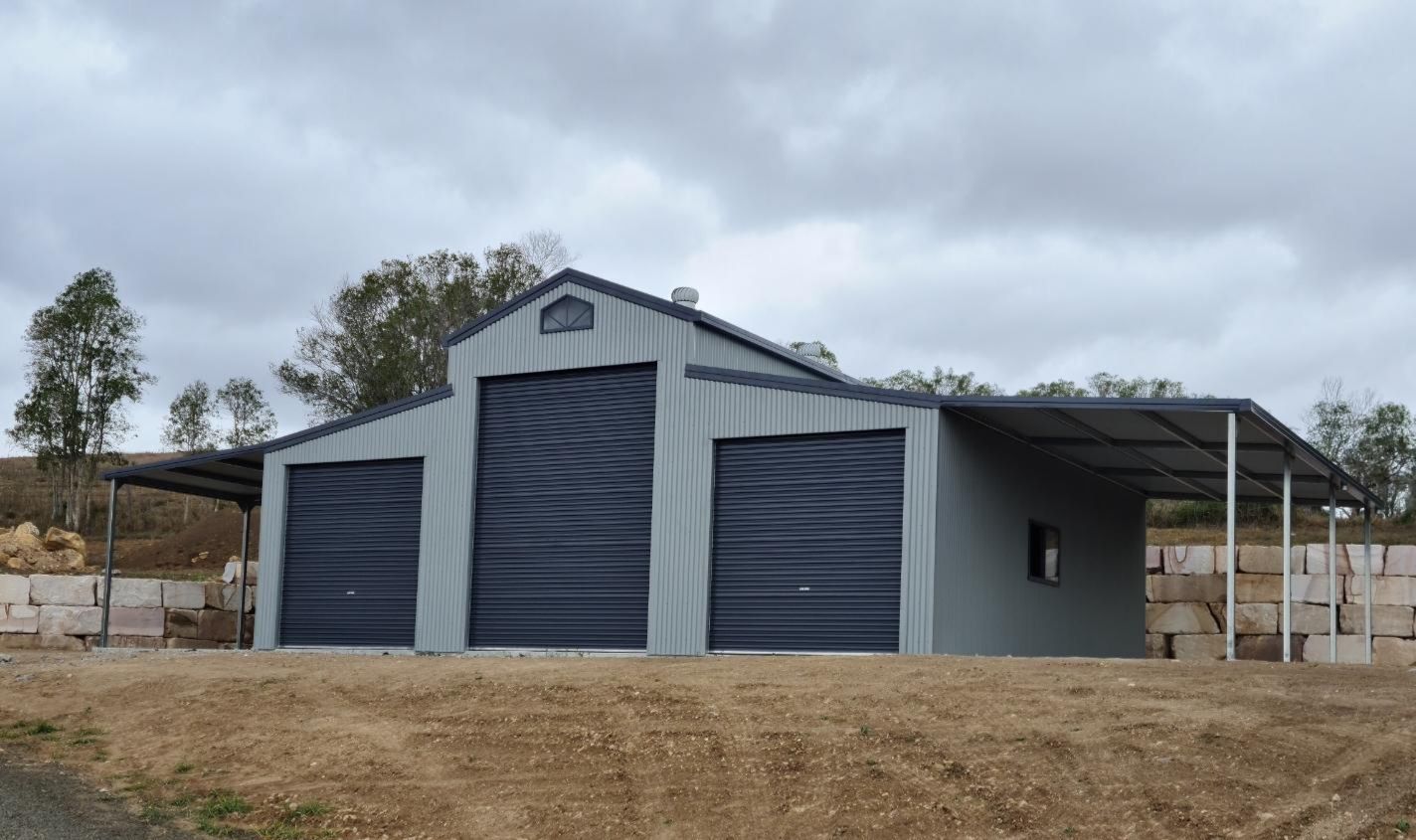 A large metal building with two garage doors and a canopy. — Just Sheds In Kunda Park, QLD