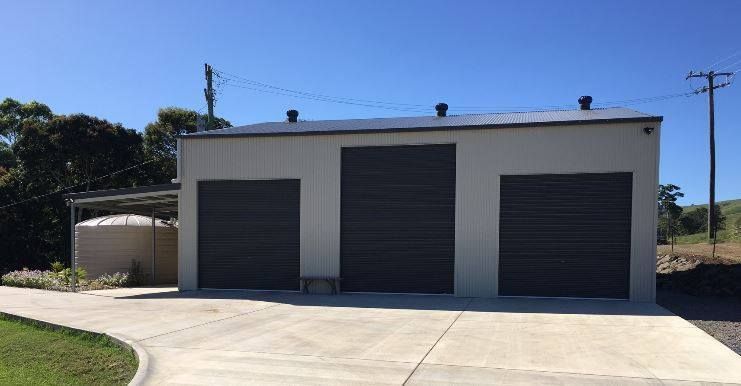 A White Garage With Three Black Garage Doors And A Concrete Driveway — Just Sheds In Kunda Park, QLD