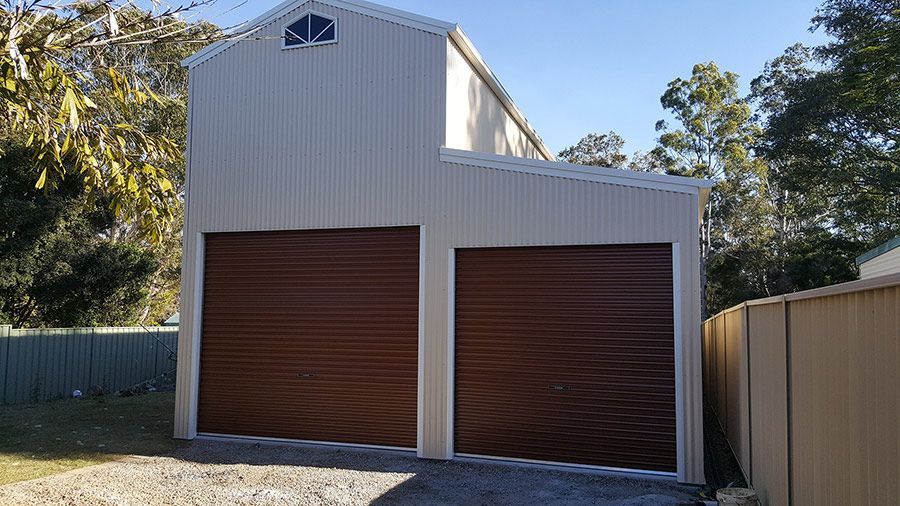 A White Garage With Two Brown Garage Doors is Next to a Fence — Just Sheds In Kunda Park, QLD