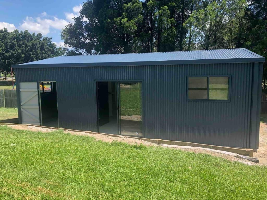 A Large Metal Building Is Sitting In The Middle Of A Lush Green Field — Just Sheds In Kunda Park, QLD