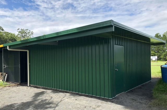 A Green Metal Building With A Roof Is Sitting On Top Of A Dirt Field — Just Sheds In Kunda Park, QLD