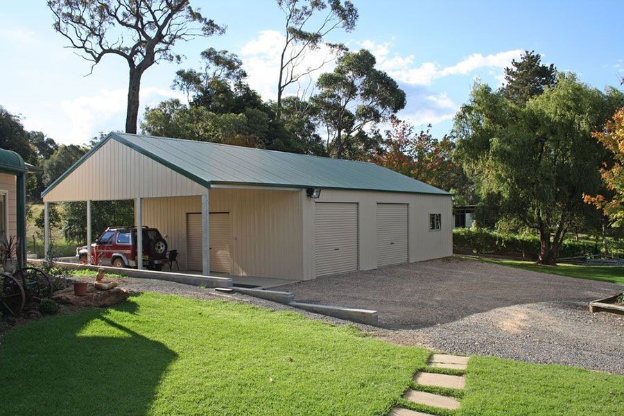 A car is parked under a carport in front of a garage.
