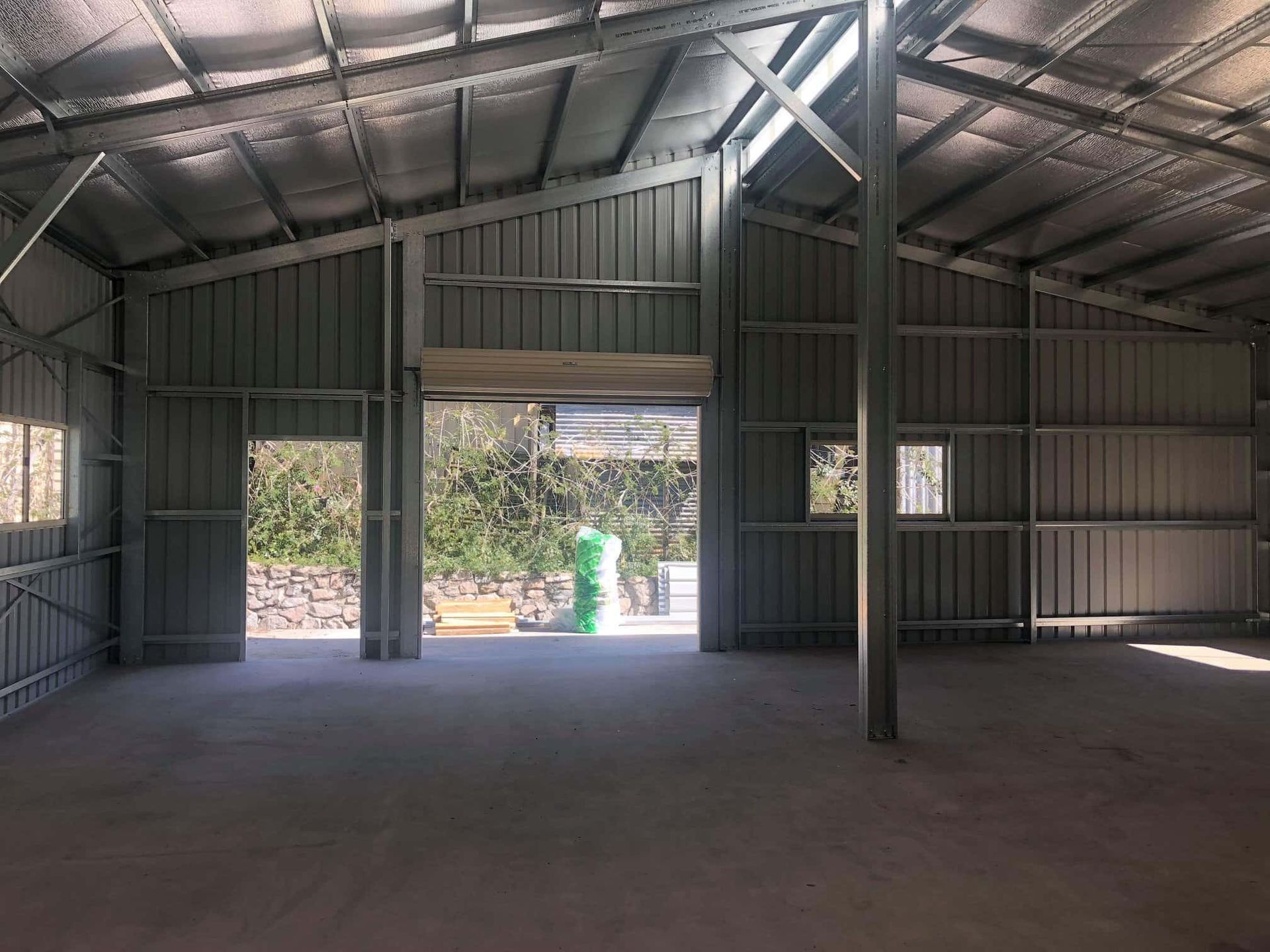 A man in a green suit is standing in an empty warehouse with the door open. — Just Sheds In Kunda Park, QLD