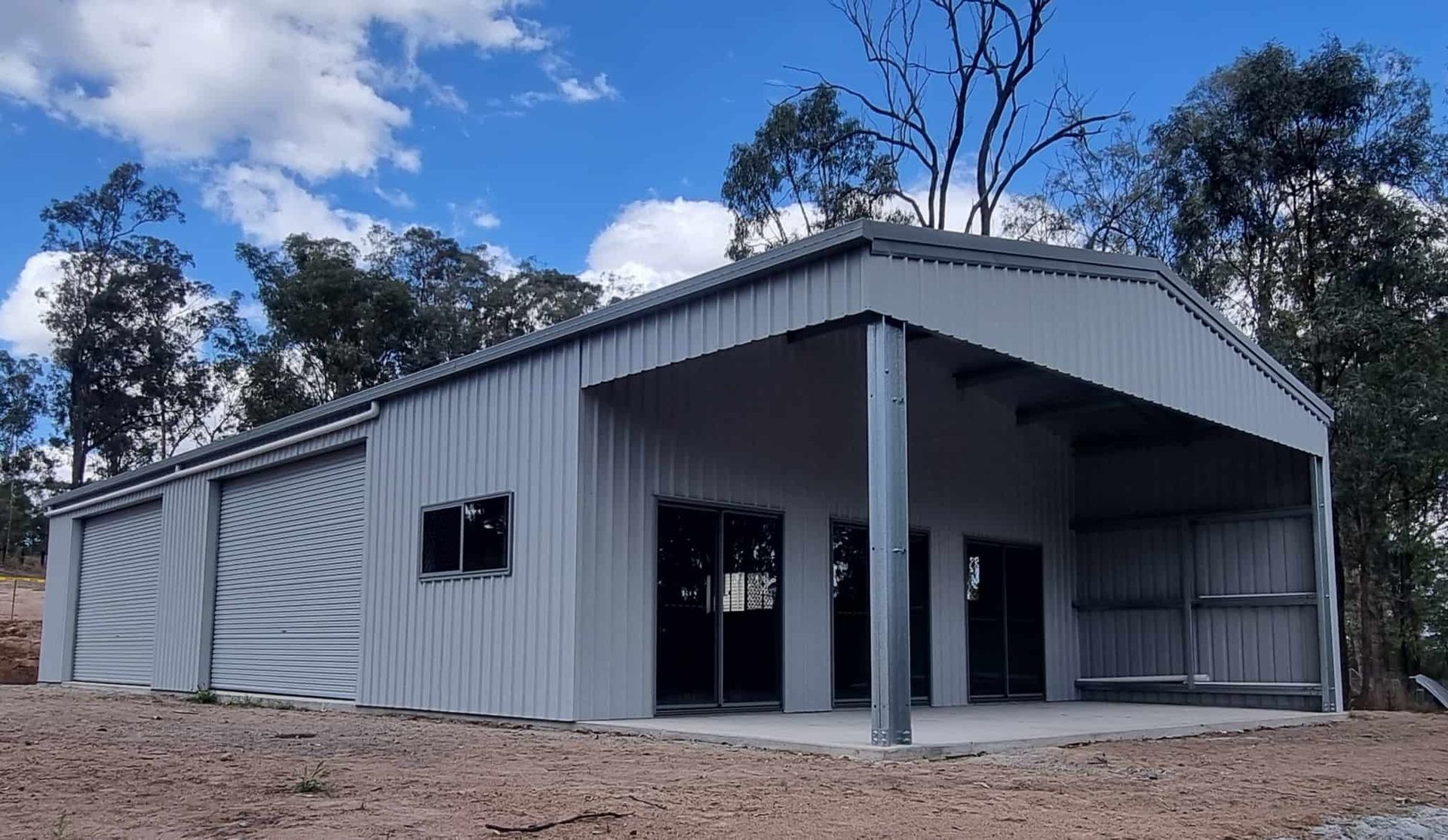 A Large Metal Building With A Porch And Trees In The Background — Just Sheds In Brendale, QLD