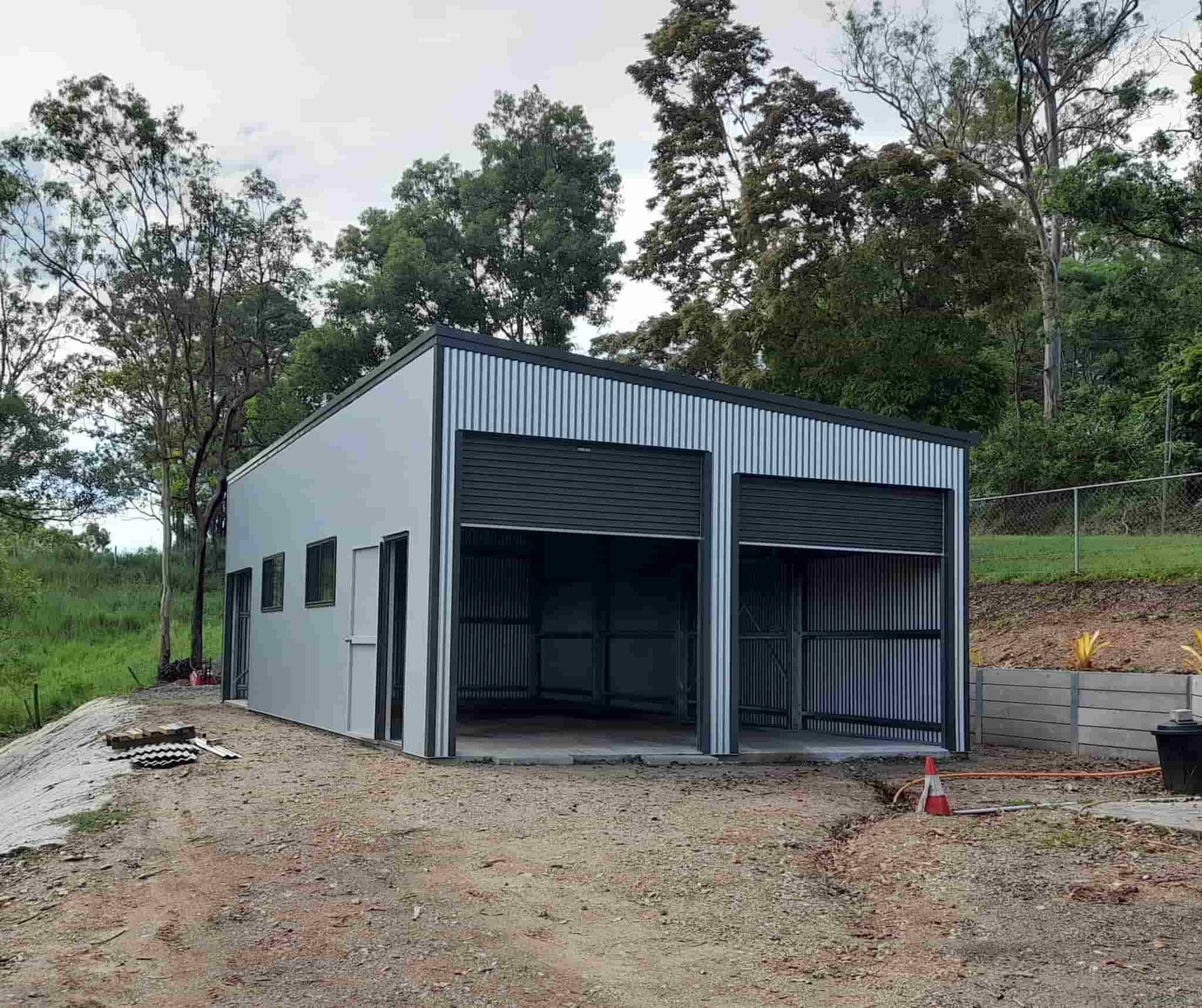 A Metal Building With Two Garage Doors Is Being Built In The Middle Of A Dirt Field — Just Sheds In Brendale, QLD