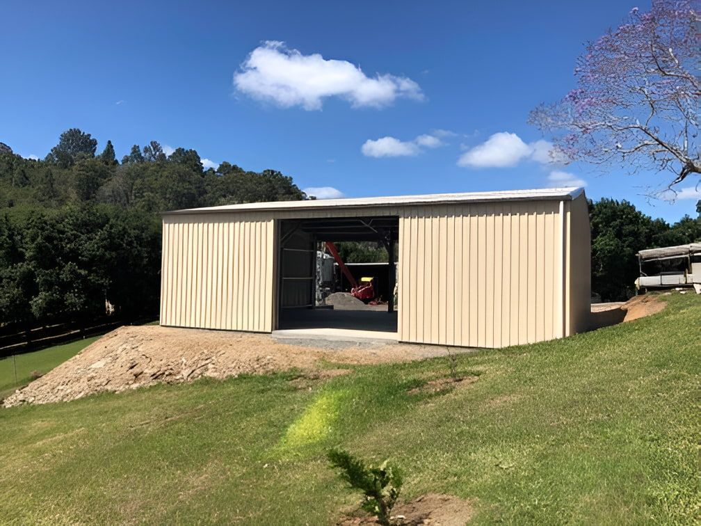 A large metal building is sitting on top of a grassy hill. — Just Sheds In Kunda Park, QLD