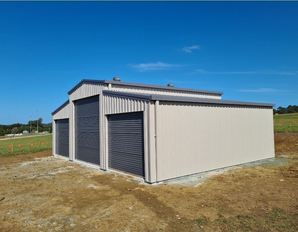 A metal building with two garage doors is sitting in the middle of a field. — Just Sheds In Kunda Park, QLD