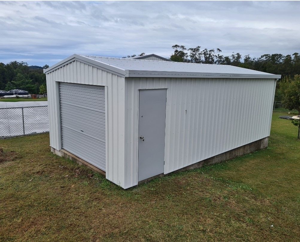 A white garage with a garage door is sitting in the middle of a grassy field. — Just Sheds In Brendale, QLD