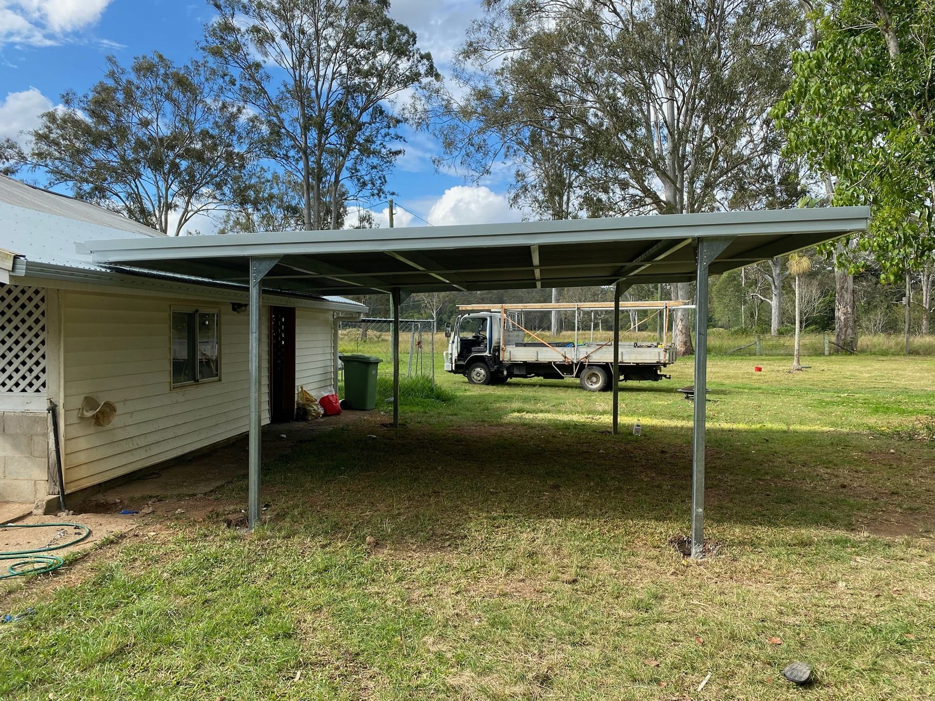 A truck is parked under a carport in front of a house. — Just Sheds In Brisbane, QLD