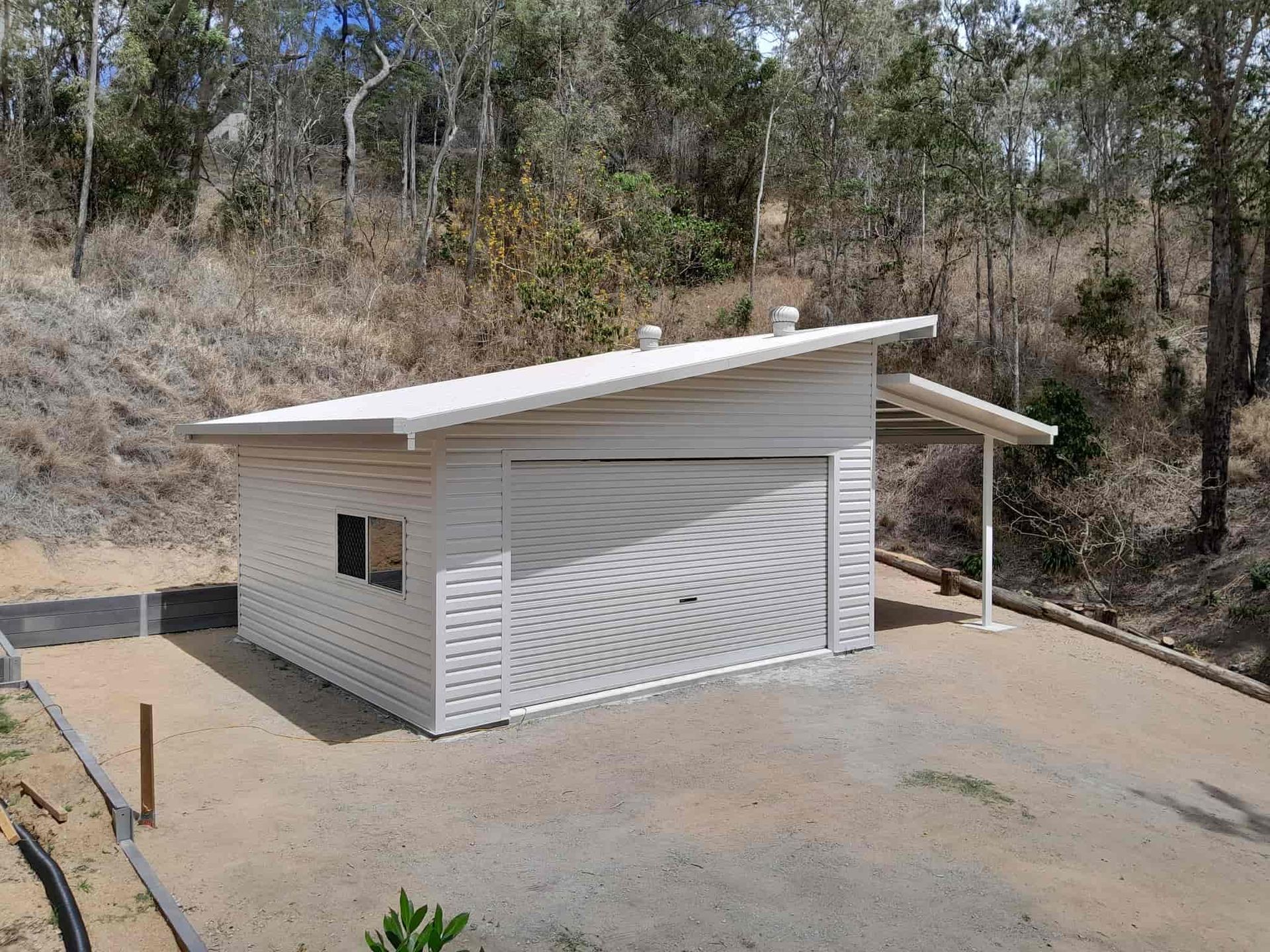A small white garage is sitting on top of a dirt hill. — Just Sheds In Kunda Park, QLD